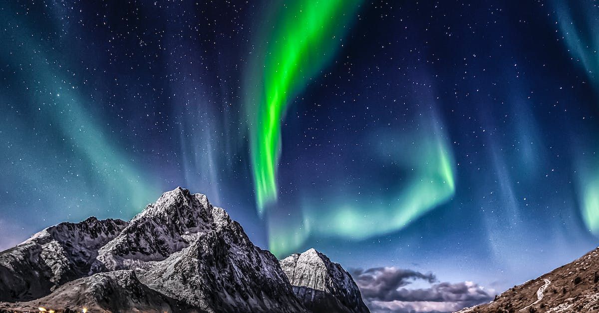 Aurora Borealis, green and white light display, over snow-capped mountains and starry night sky.