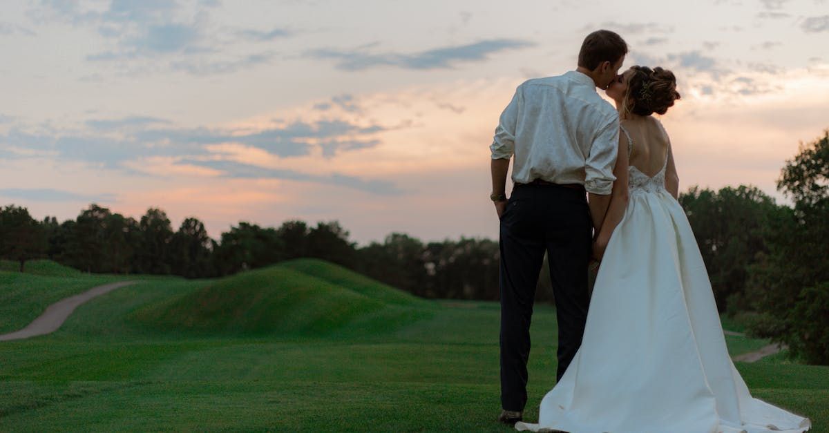 A bride and groom are kissing in a field at sunset.