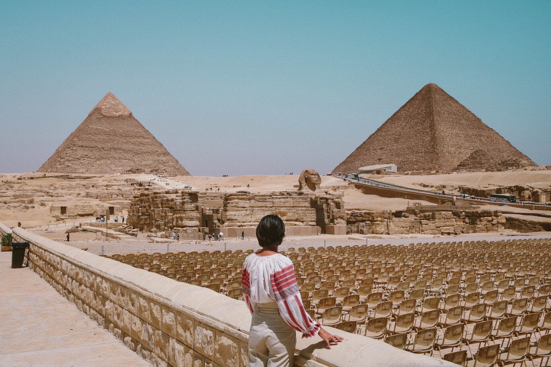 A woman is standing in front of two pyramids in the desert.
