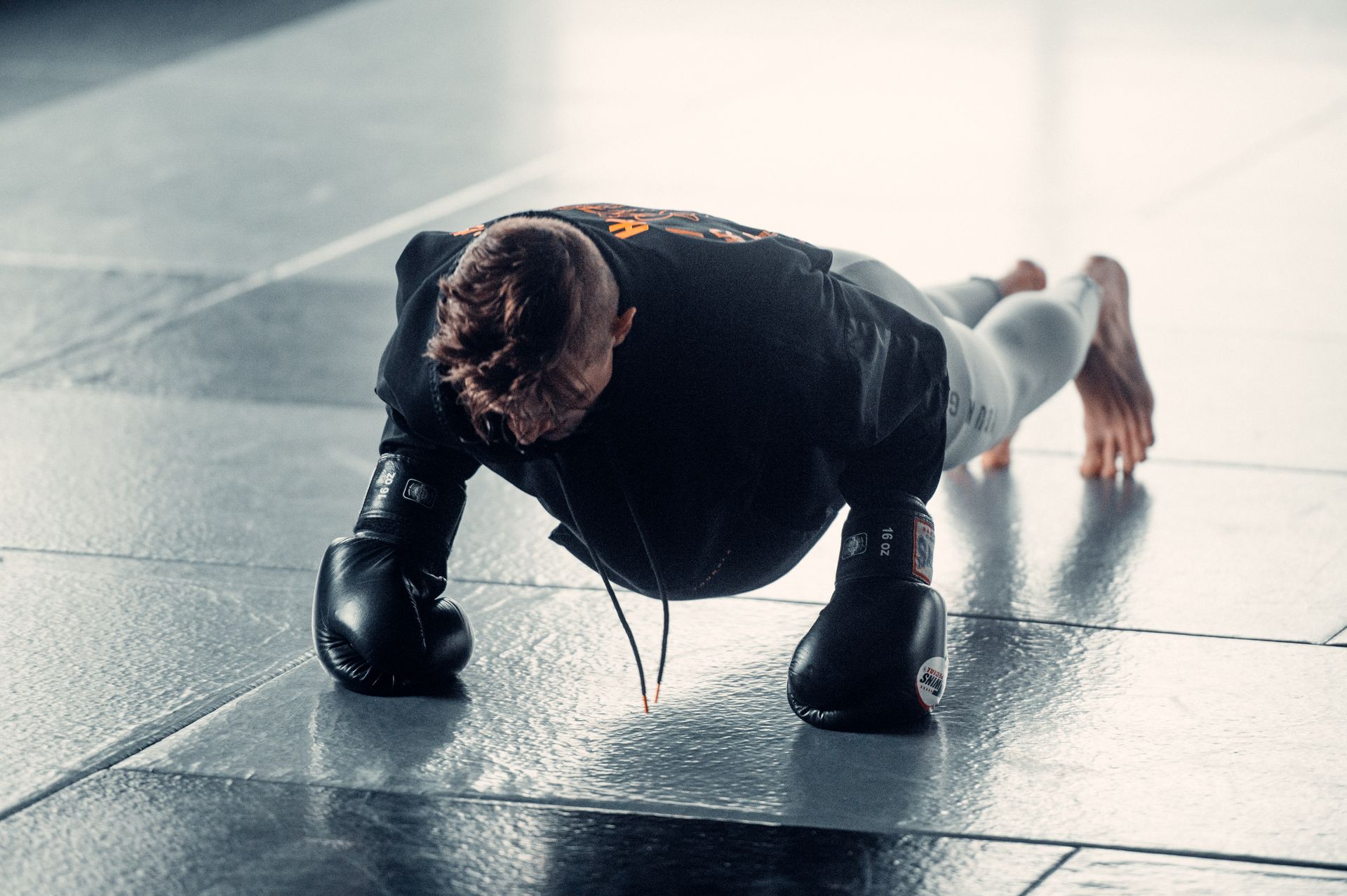 A man wearing boxing gloves is doing push ups on the floor.