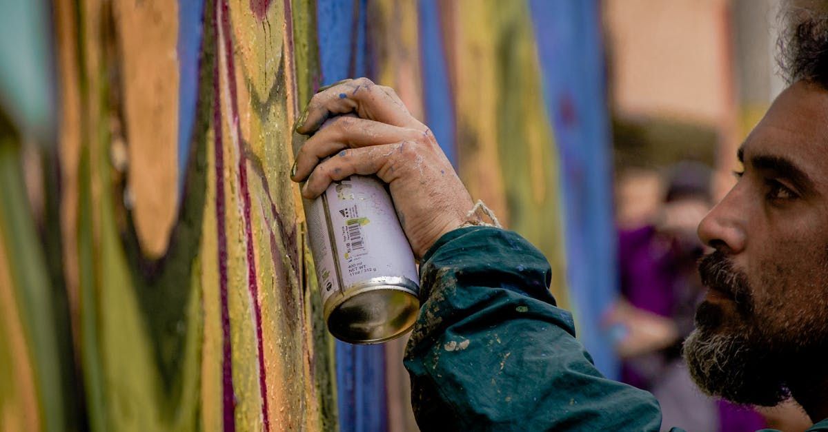 Un hombre con las manos sucias rocía pintura sobre un mural colorido con una lata de aerosol.
