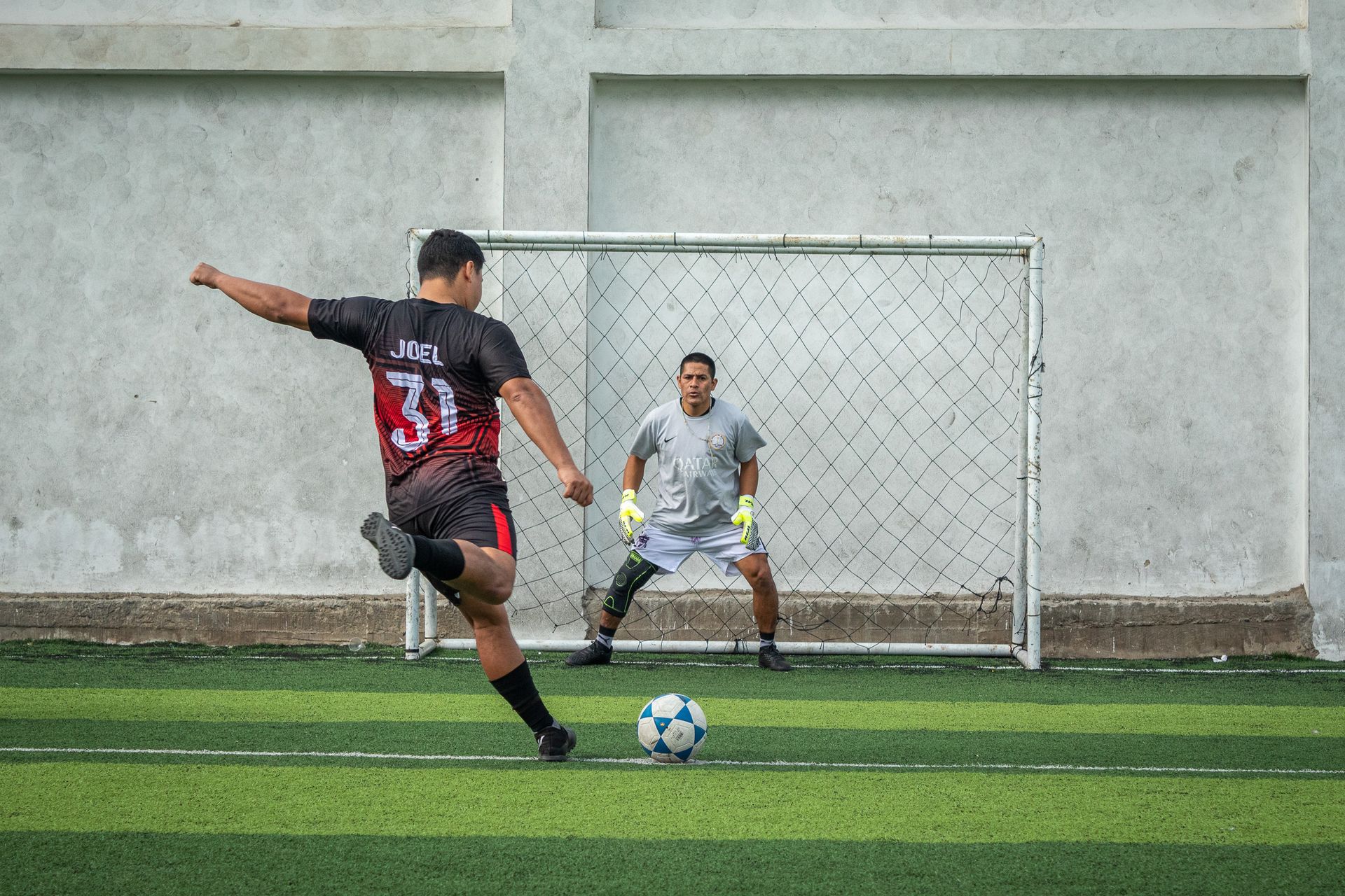 A man is kicking a soccer ball at a goal while another man watches.