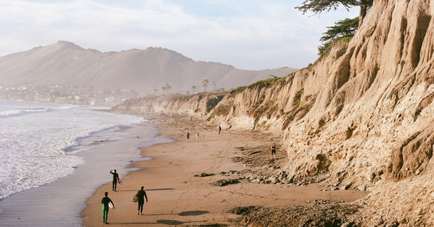 A group of people are walking on a beach near a cliff.
