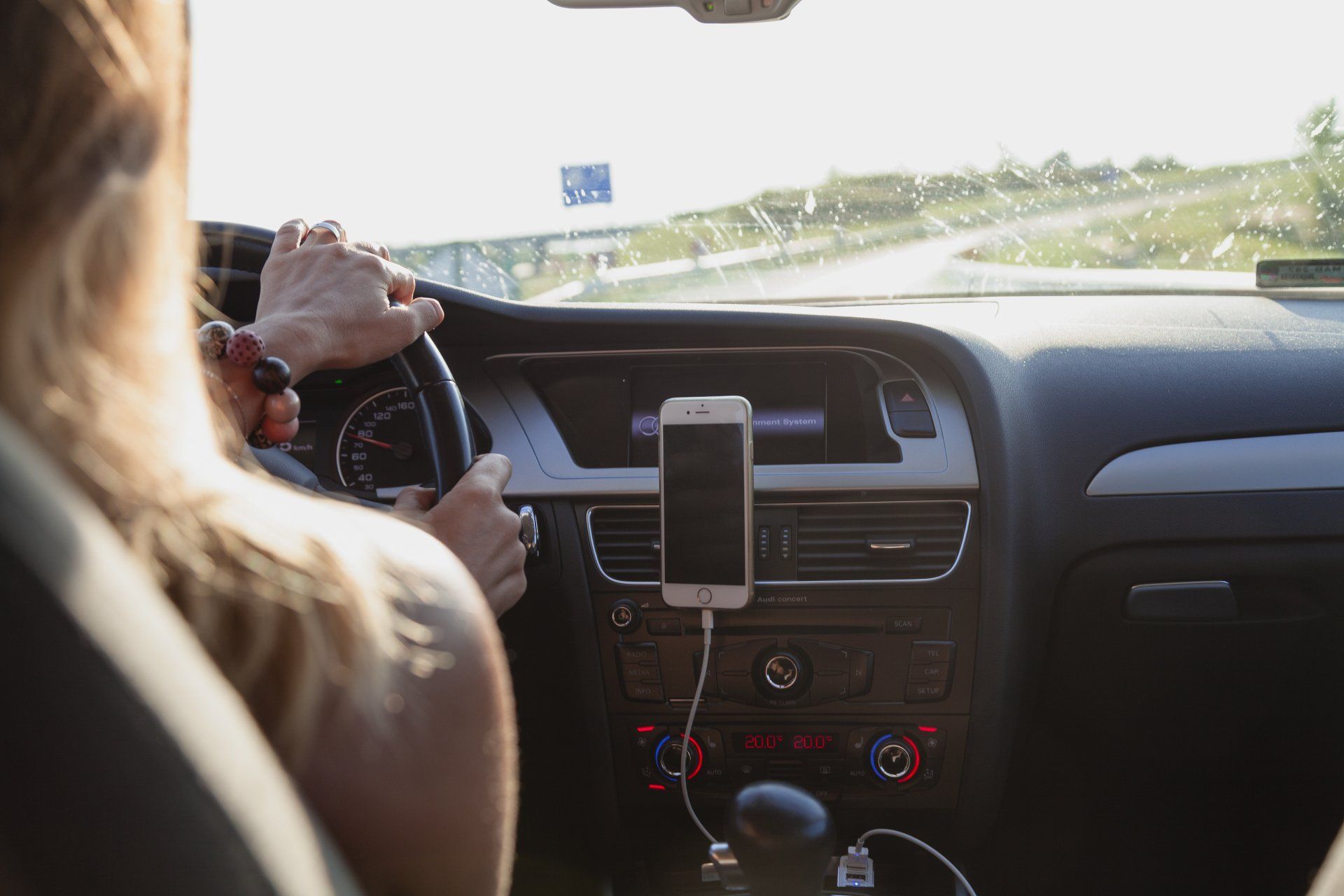 a woman is driving a car with a cell phone plugged into the dashboard .