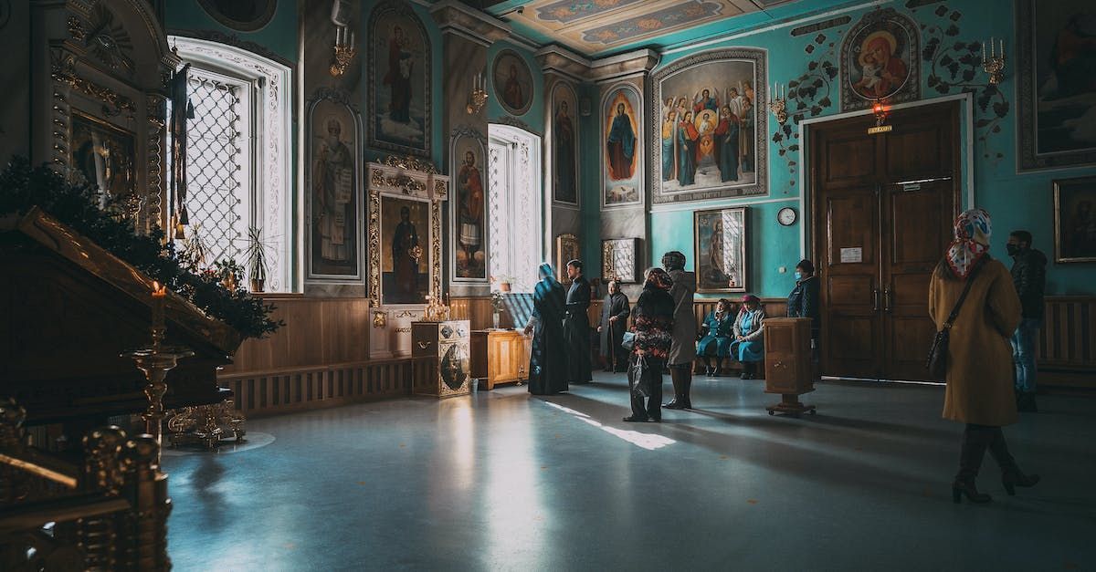 Visitors in a grand museum hall with ornate murals, large paintings, and a chandelier