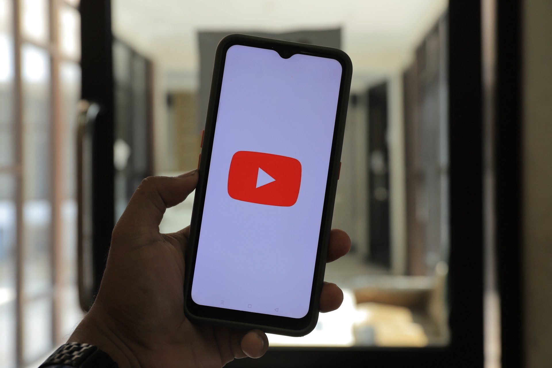 Hand holding a smartphone displaying the YouTube logo in a blurred indoor hallway