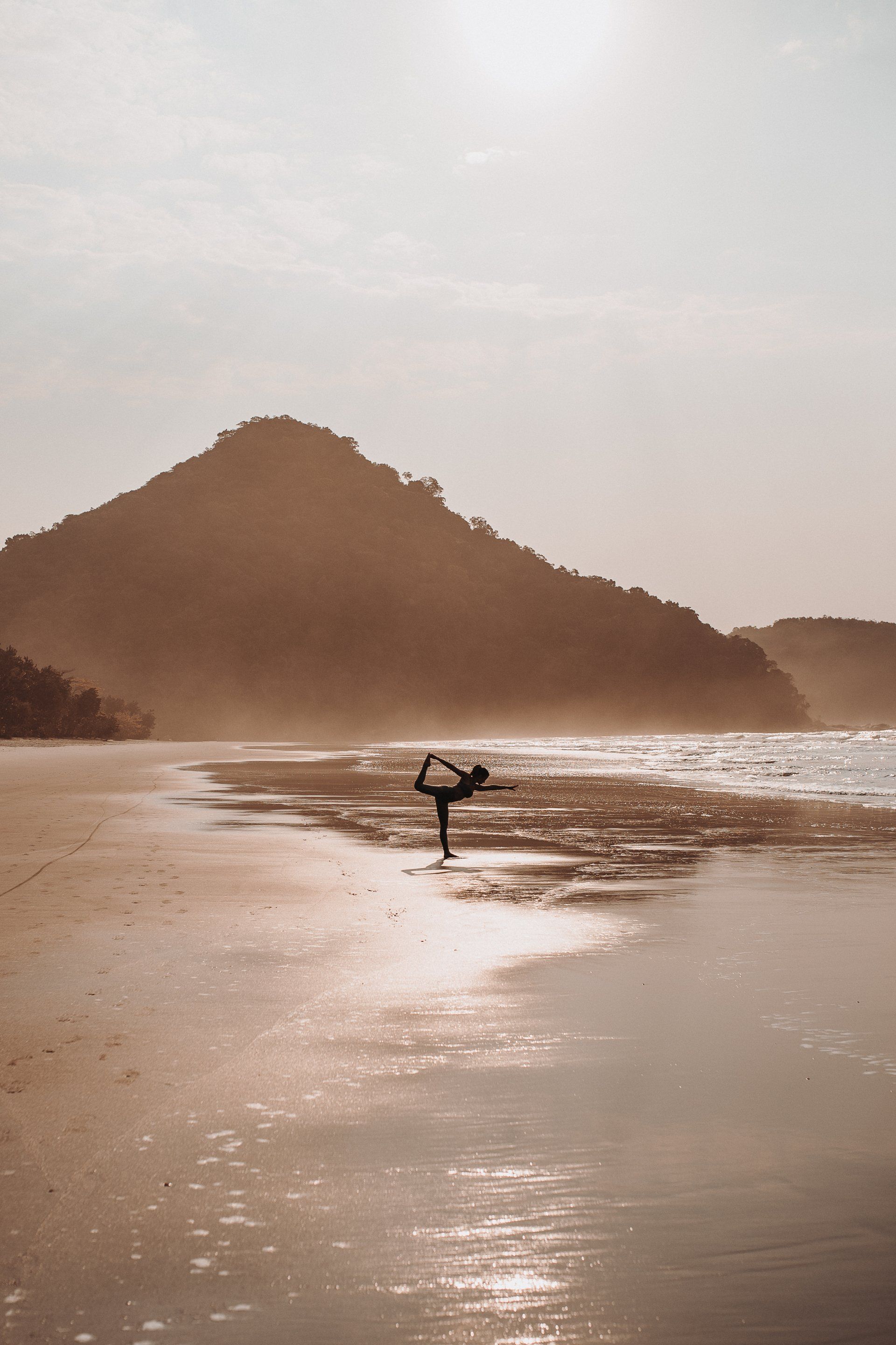 A woman is doing yoga on the beach at sunset.