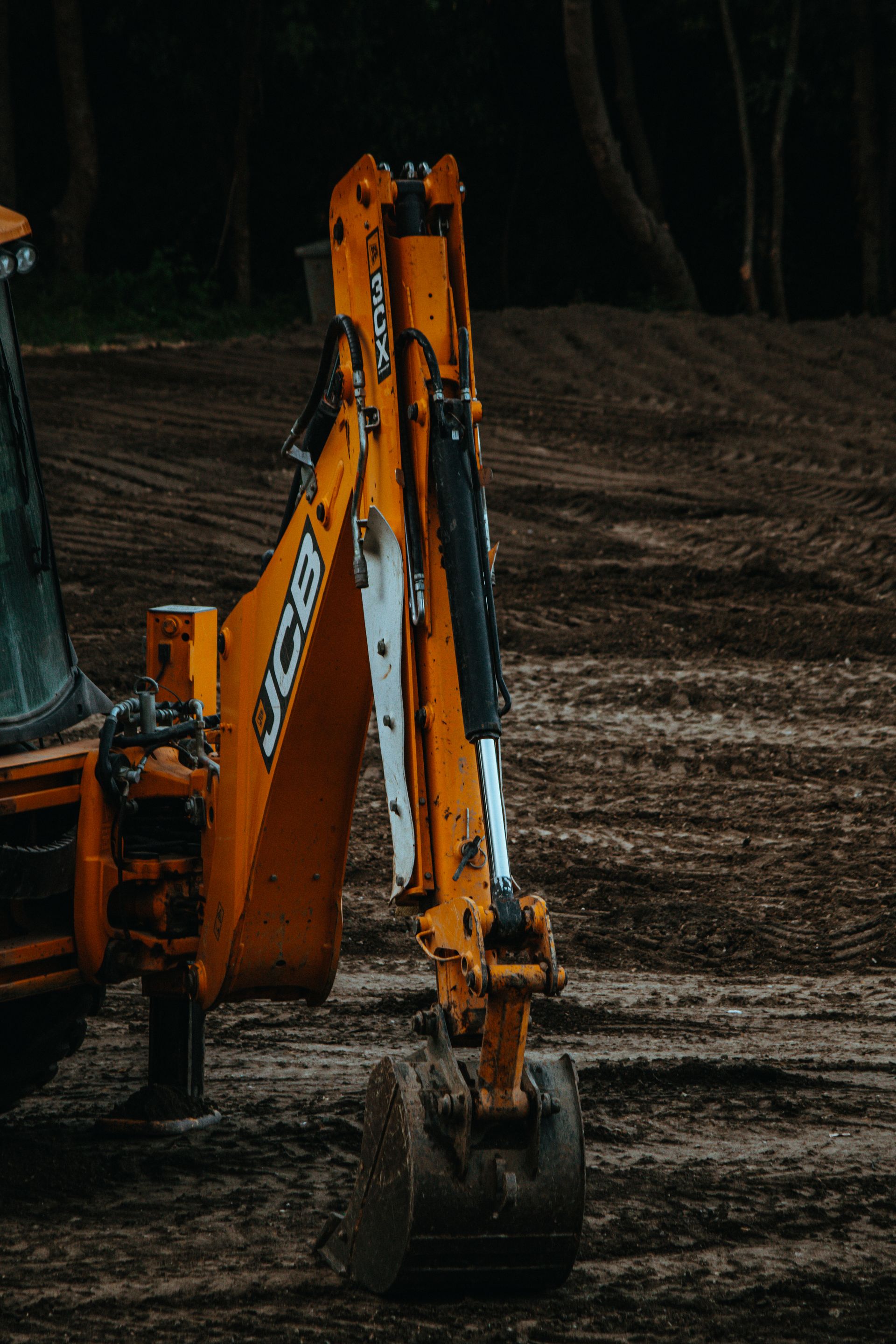 Yellow excavator arm with bucket extended over dark dirt.