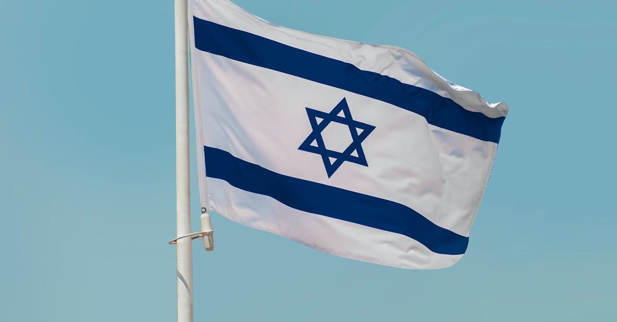 Israeli flag waving against a blue sky, featuring a white background, blue stripes, and a blue Star of David.