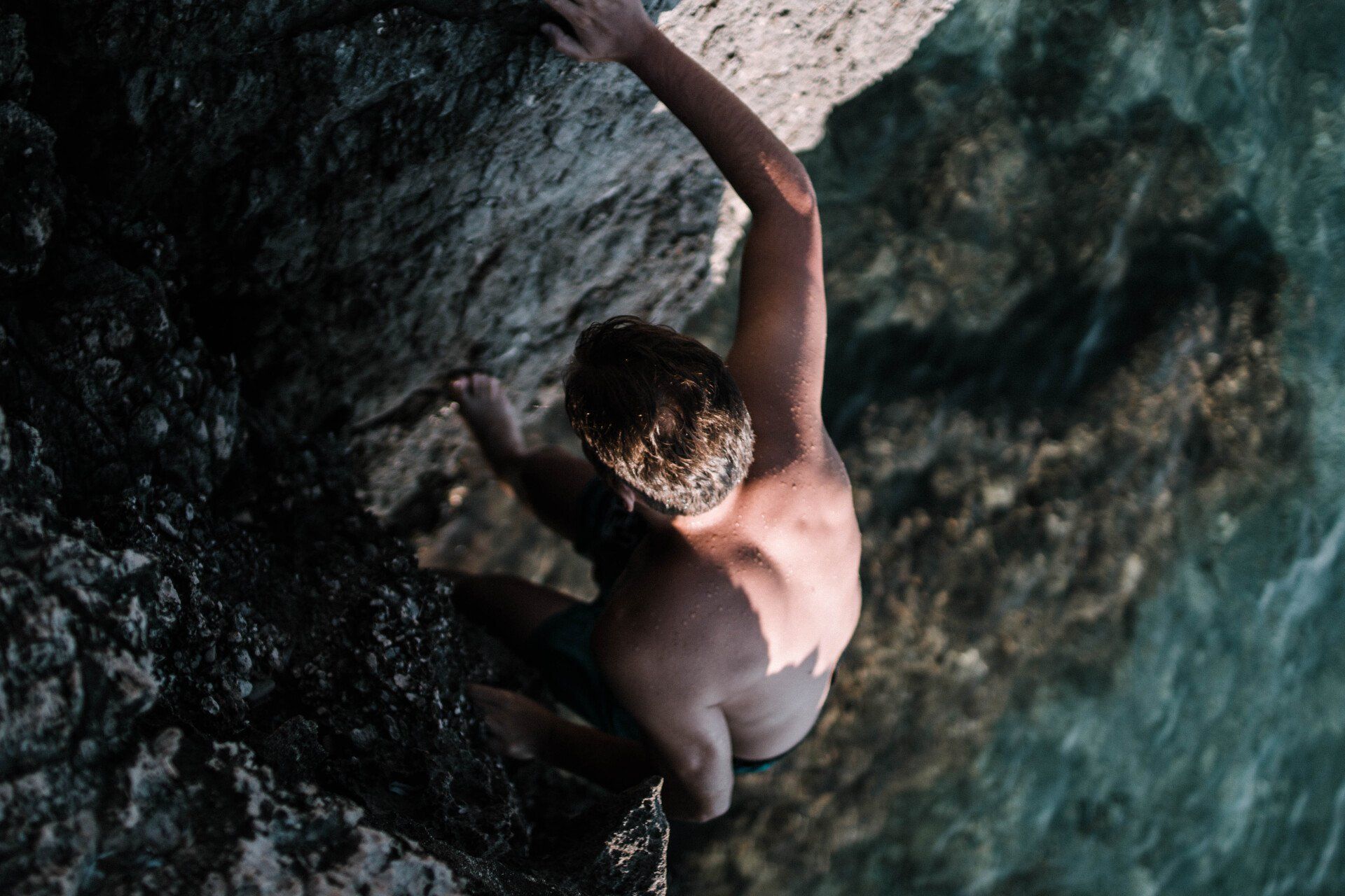 Ein Kletterer am Felsen, unter ihm blaues Wasser