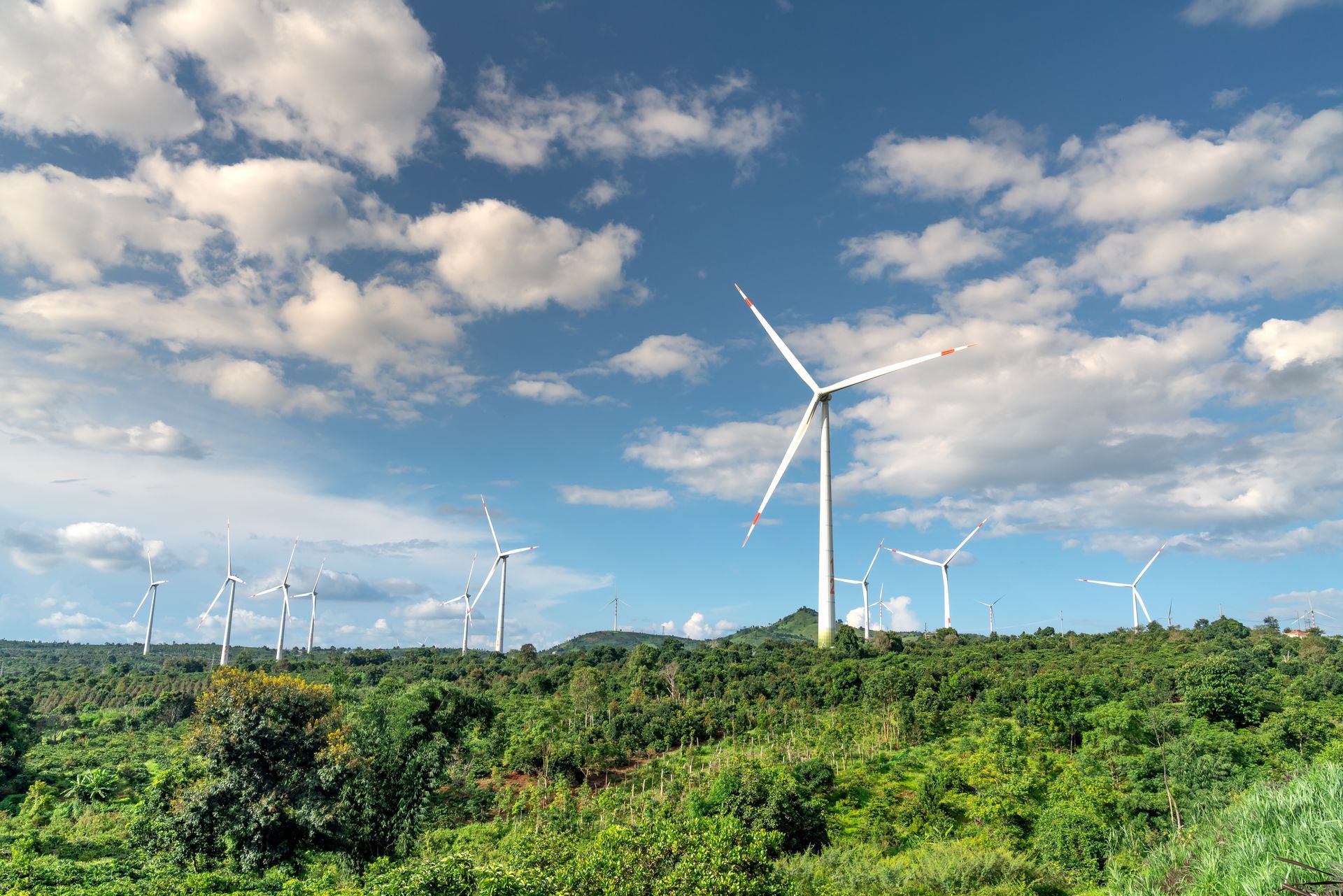 Wind turbines above green hills under a blue sky with clouds