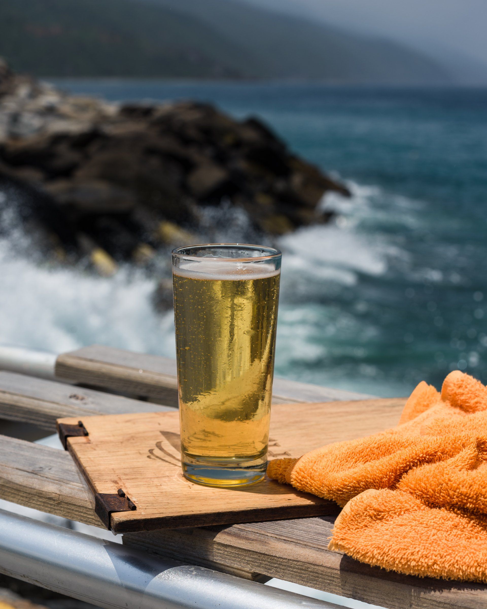 A glass of beer is sitting on a wooden tray next to fried fish.