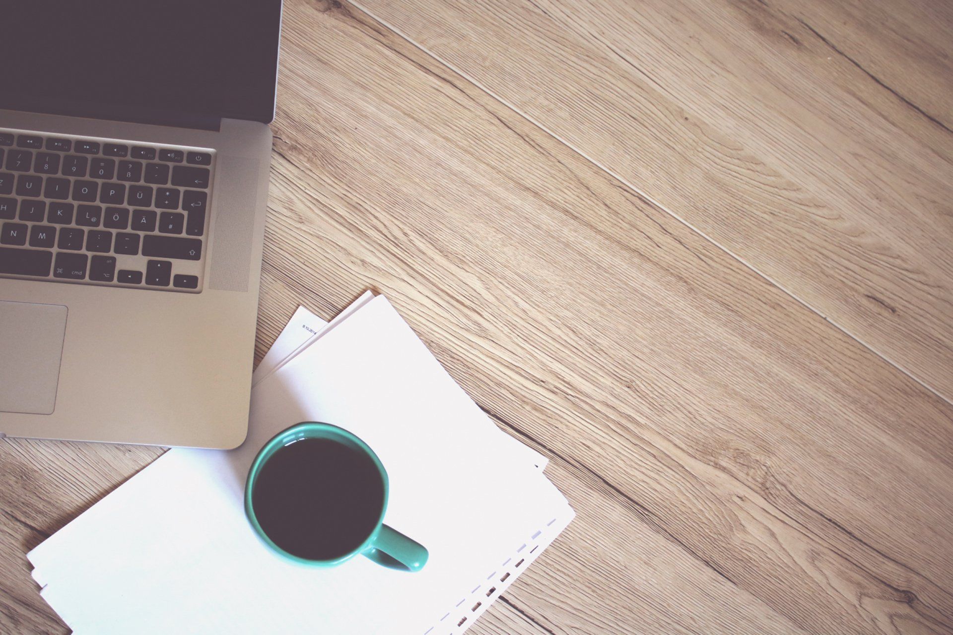 A laptop and a cup of coffee are on a wooden table.