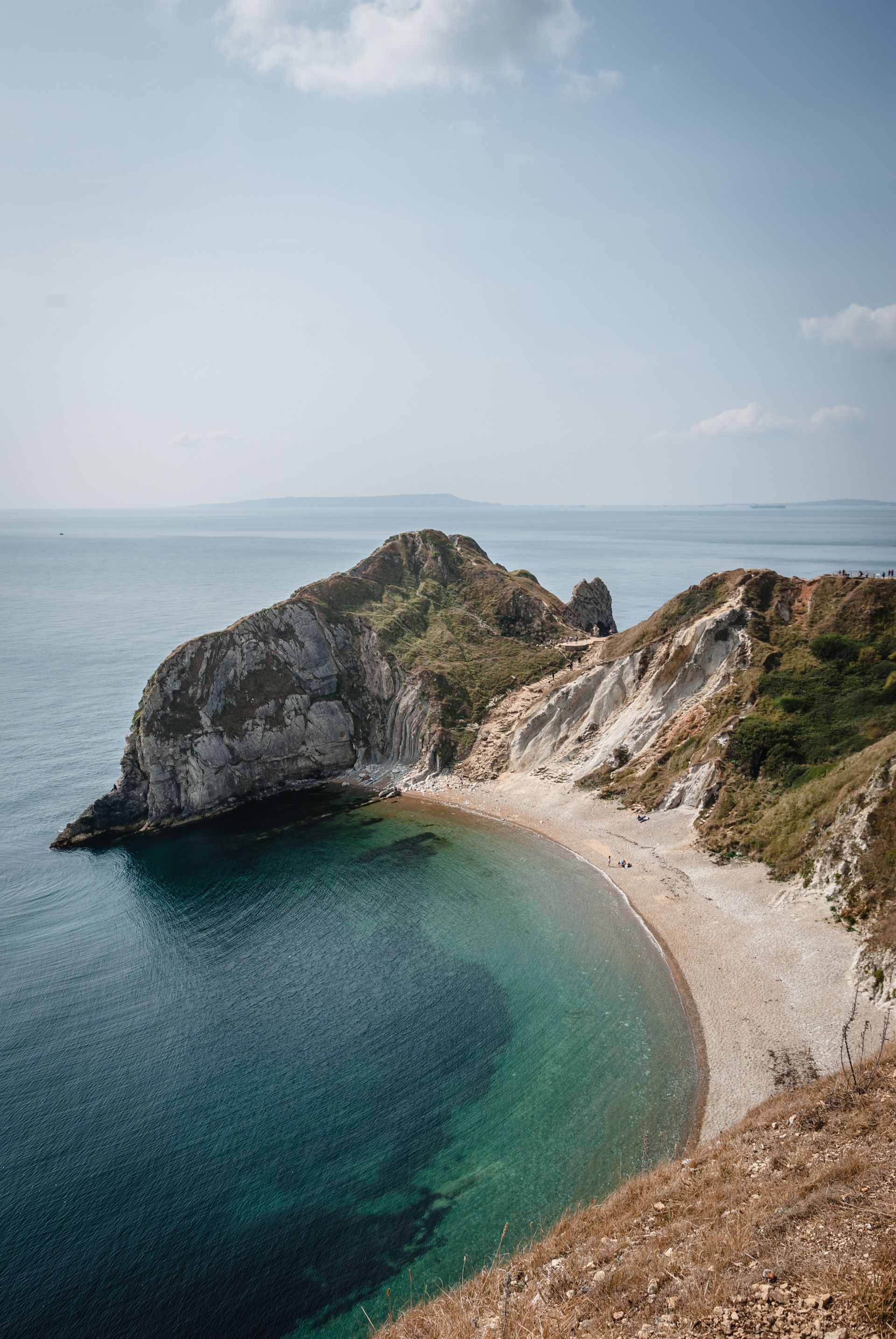a large body of water with a cliff in the background and a beach in the foreground .