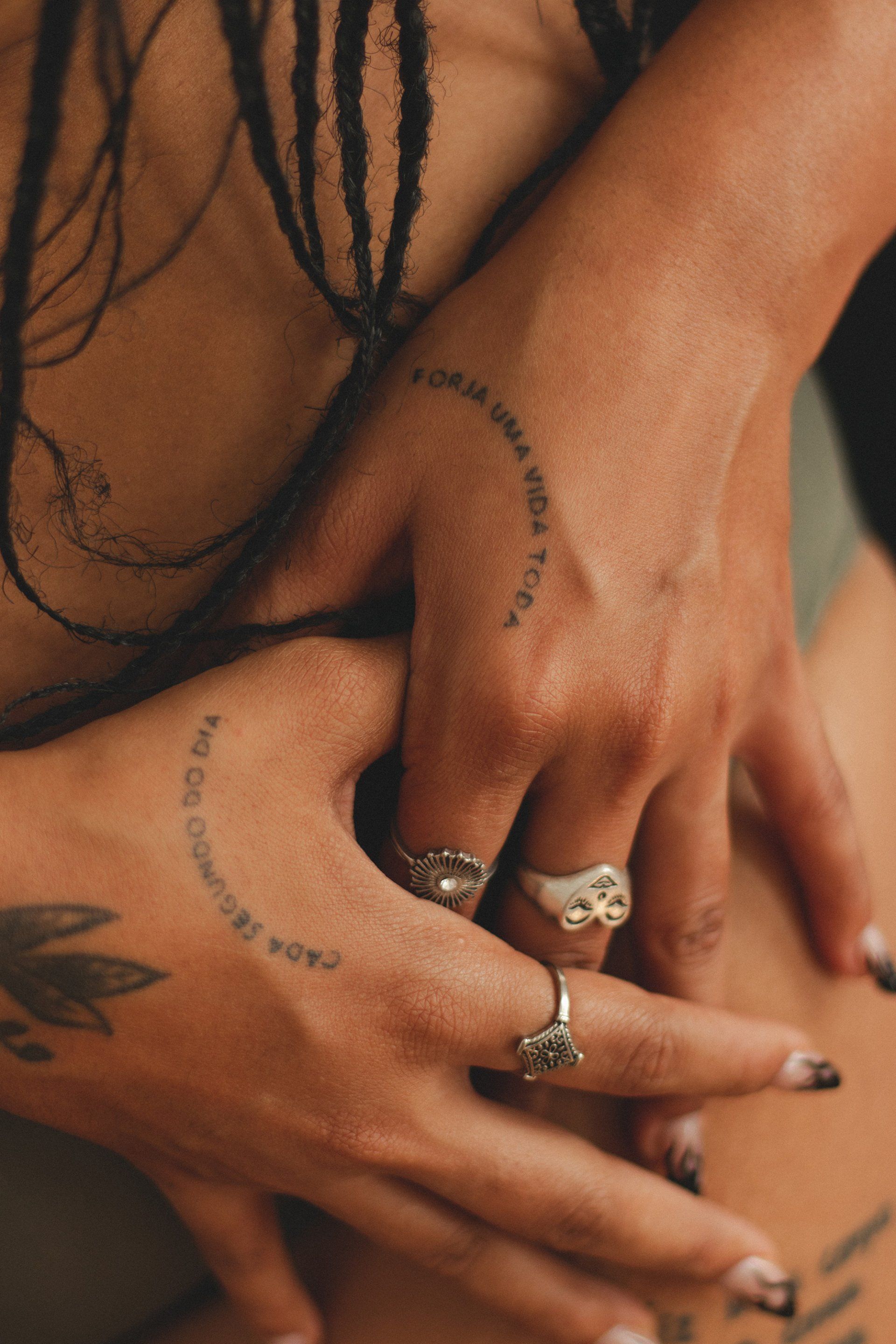 Close-up of stacked hands with rings and small tattoos on a warm-toned background