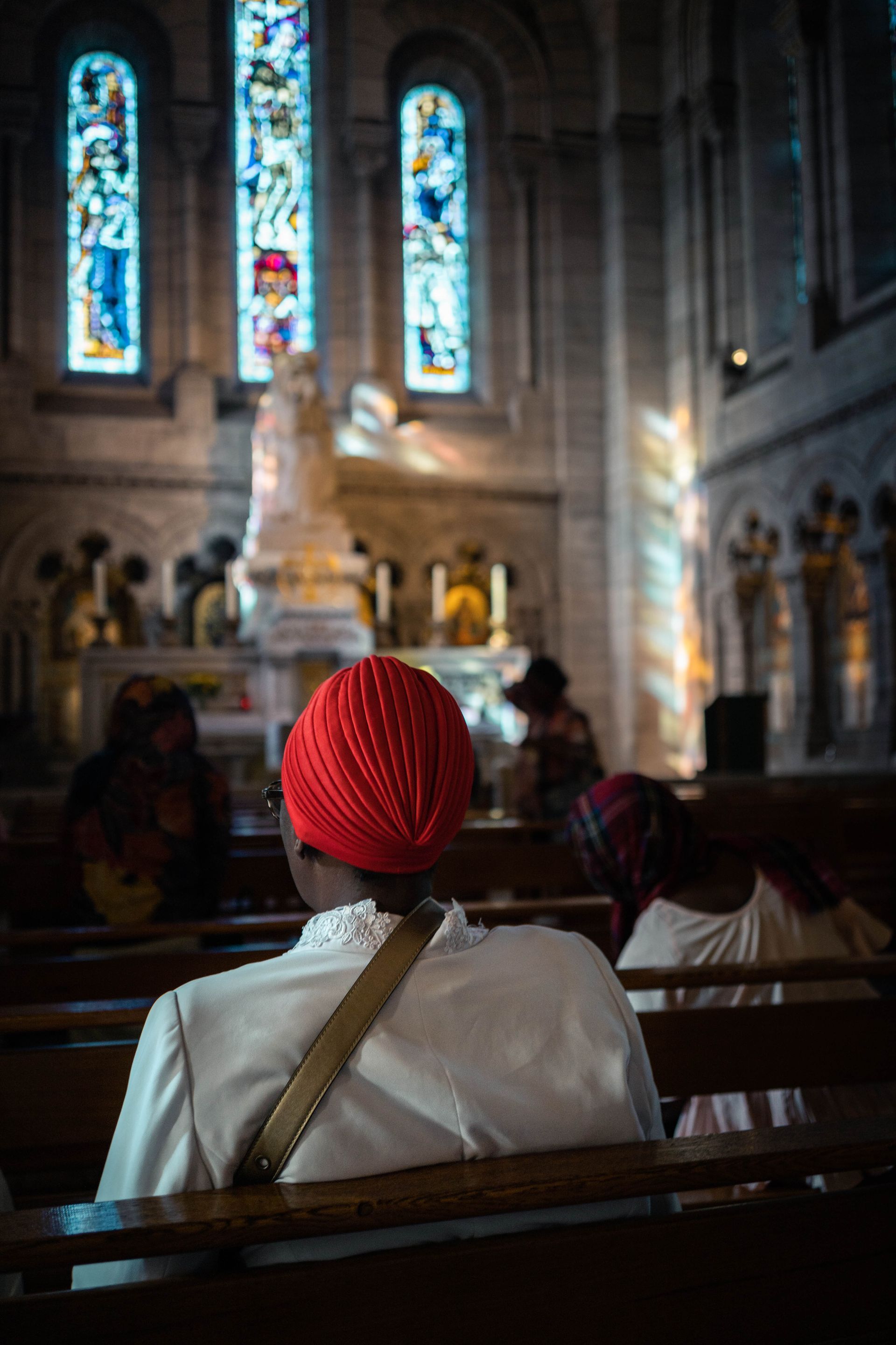 A woman wearing a red turban is sitting on a bench in a church.