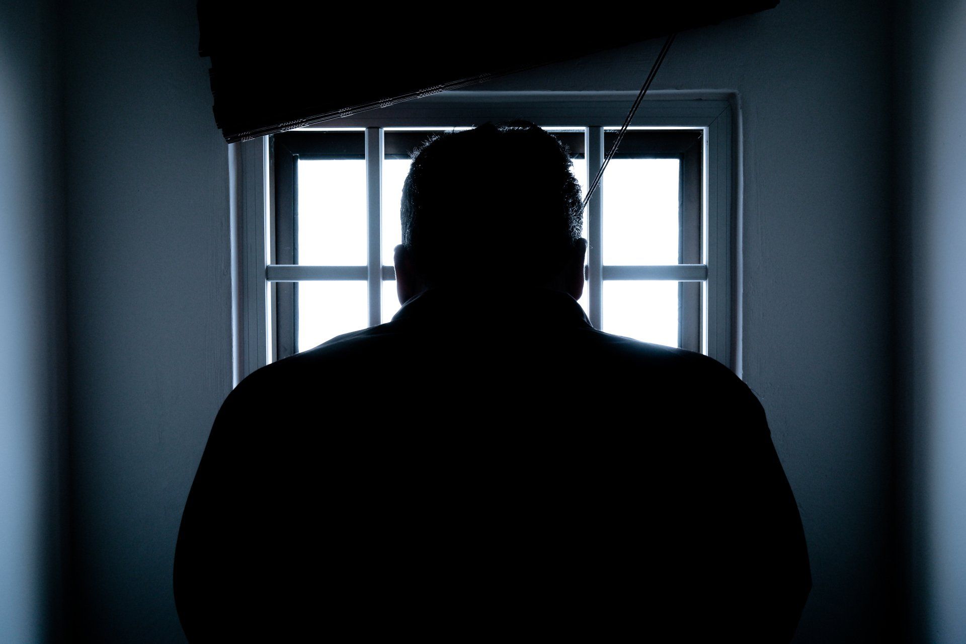 Silhouette einer Person, die in einem dunklen Raum vor einem hellen Fenster steht