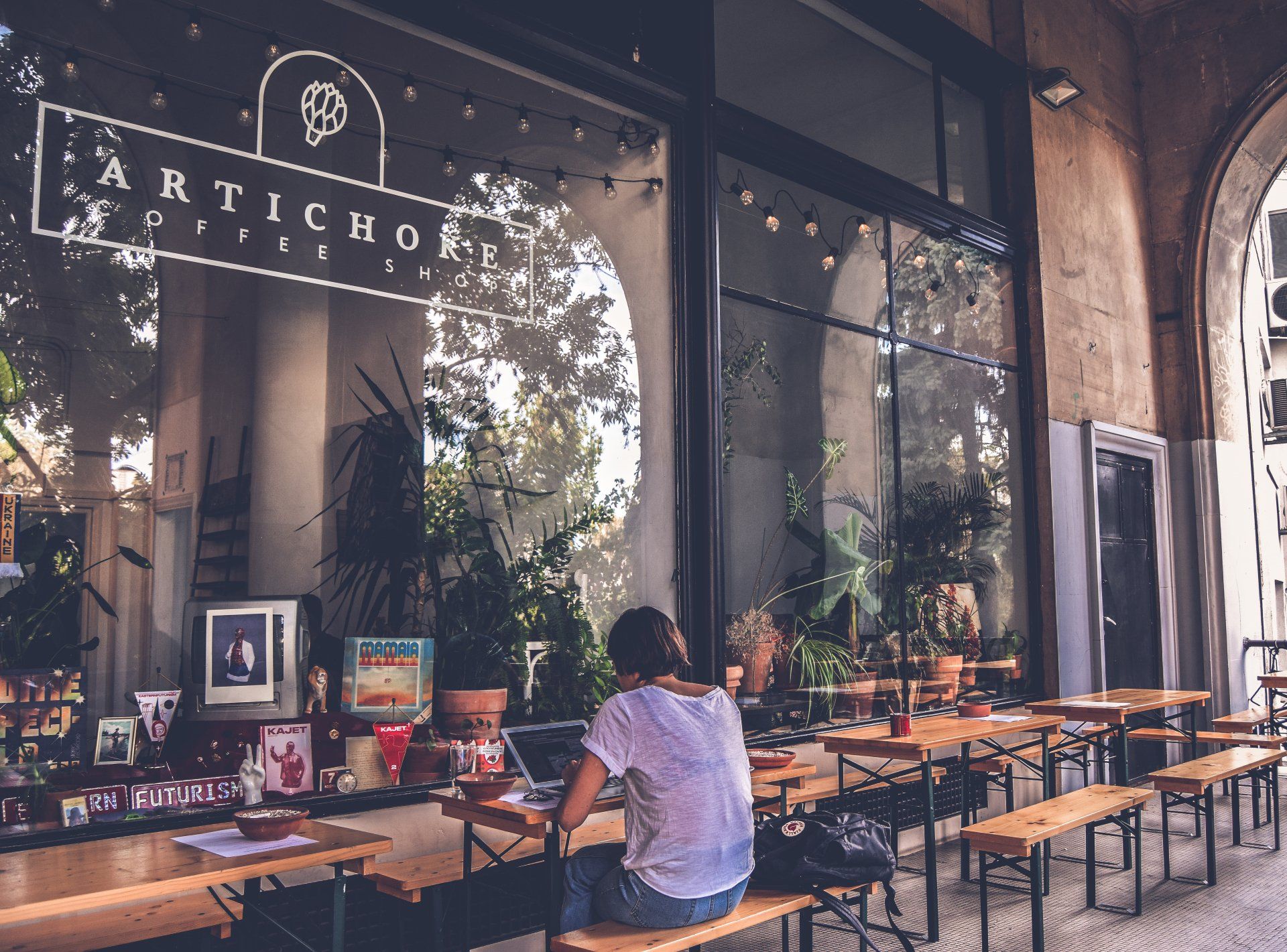 A woman sits at a table in front of an artichoke pizza restaurant