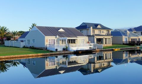 Houses with gray roofs and white trim line a calm waterway, reflections visible.