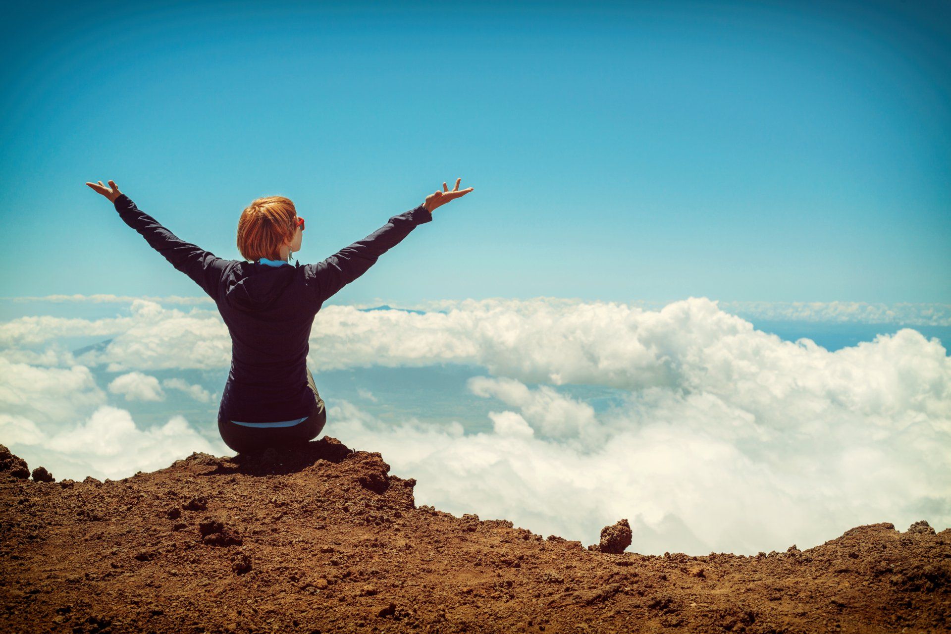 A woman is sitting on top of a mountain with her arms outstretched.