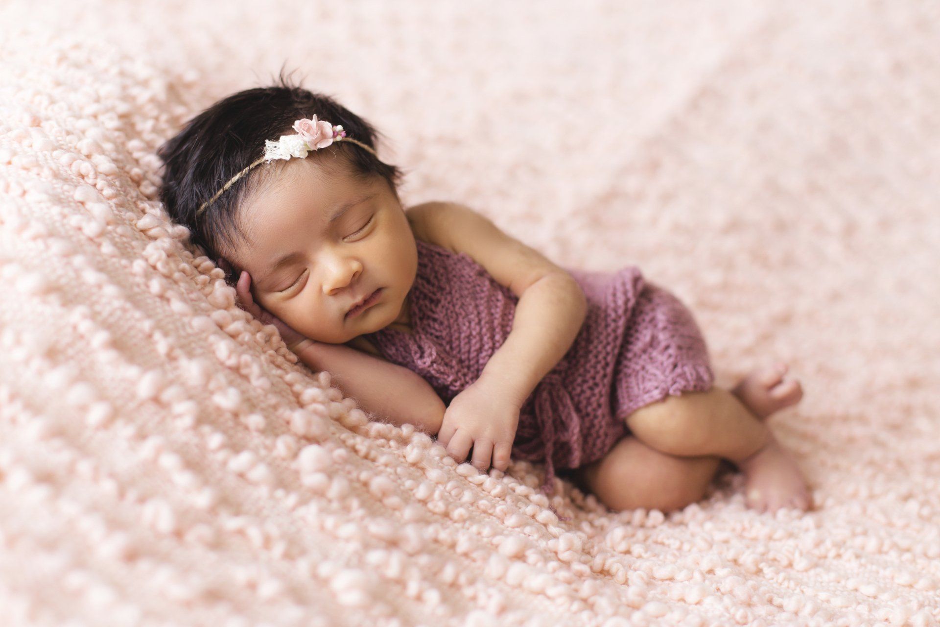 Uma menina recém-nascida está dormindo em um cobertor rosa.