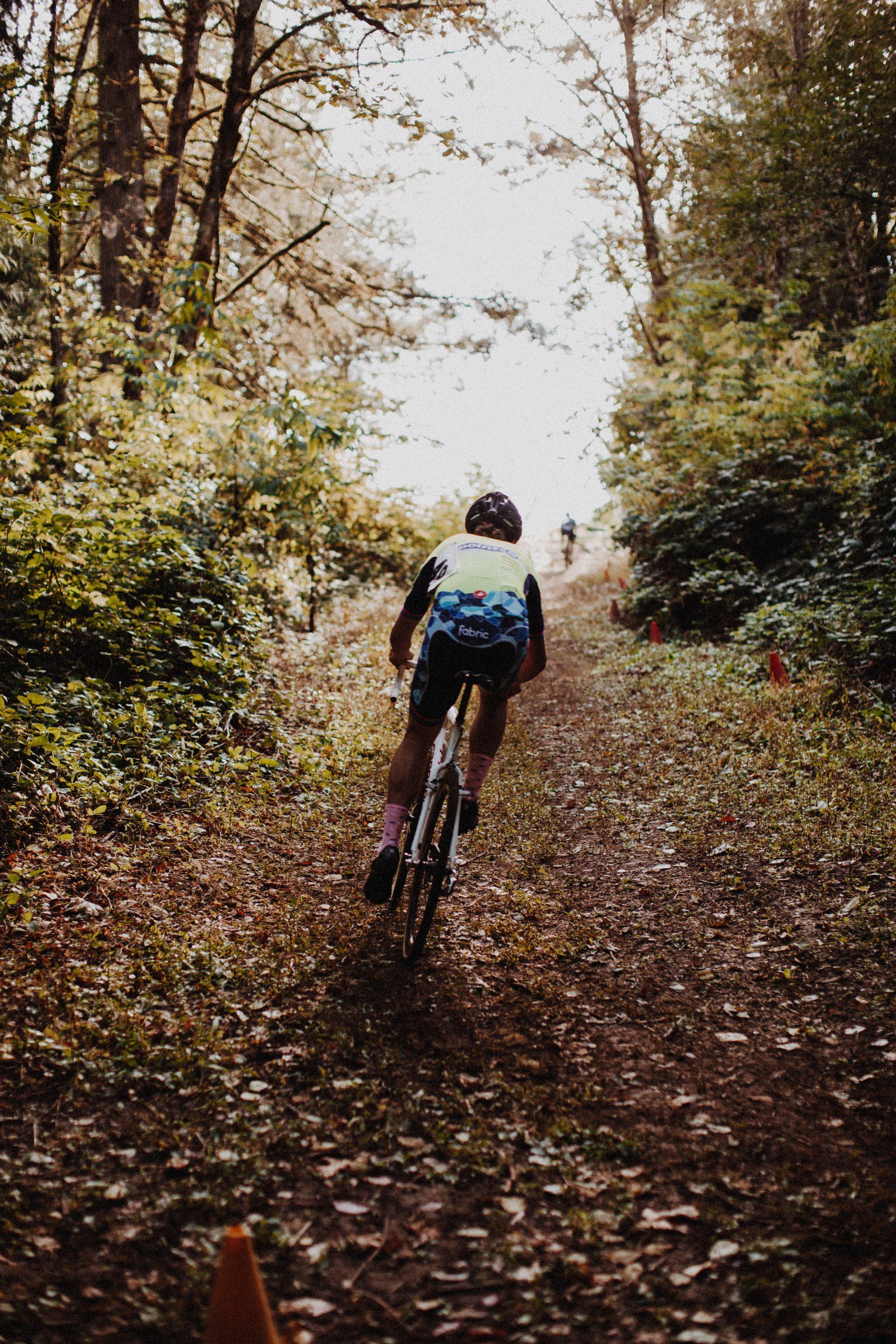 Cyclist riding uphill on a dirt path through a forest. Overcast day.