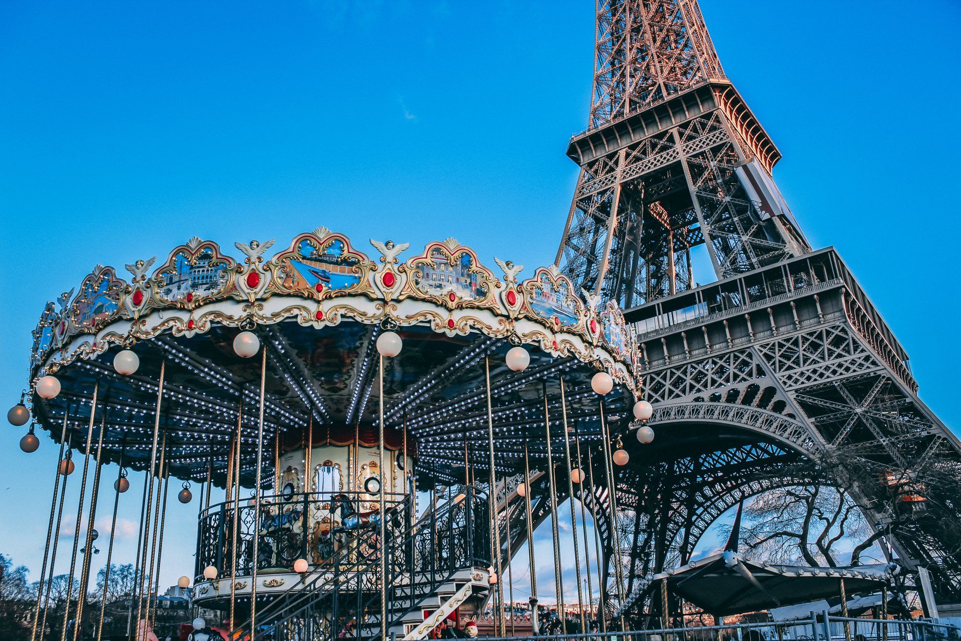 A vintage-style carousel sits in the foreground with the Eiffel Tower rising prominently against a clear blue sky.