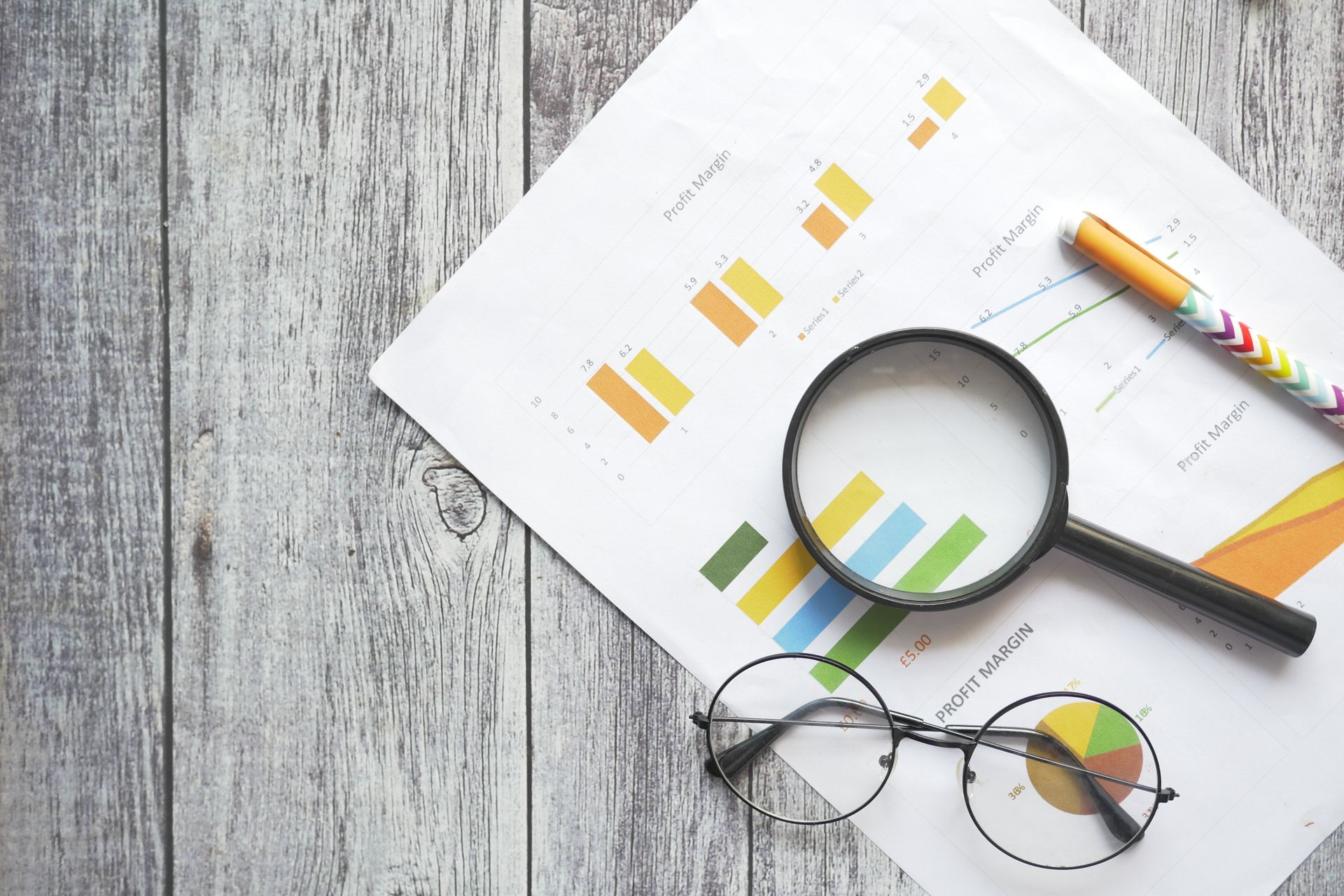 A magnifying glass is sitting on top of a piece of paper with a pen and glasses.