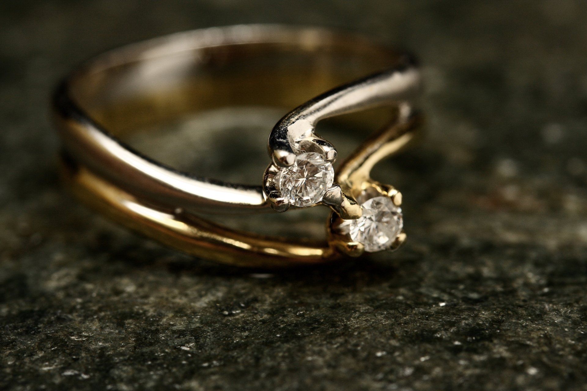 Two-toned gold ring with two diamonds set on a textured green surface.