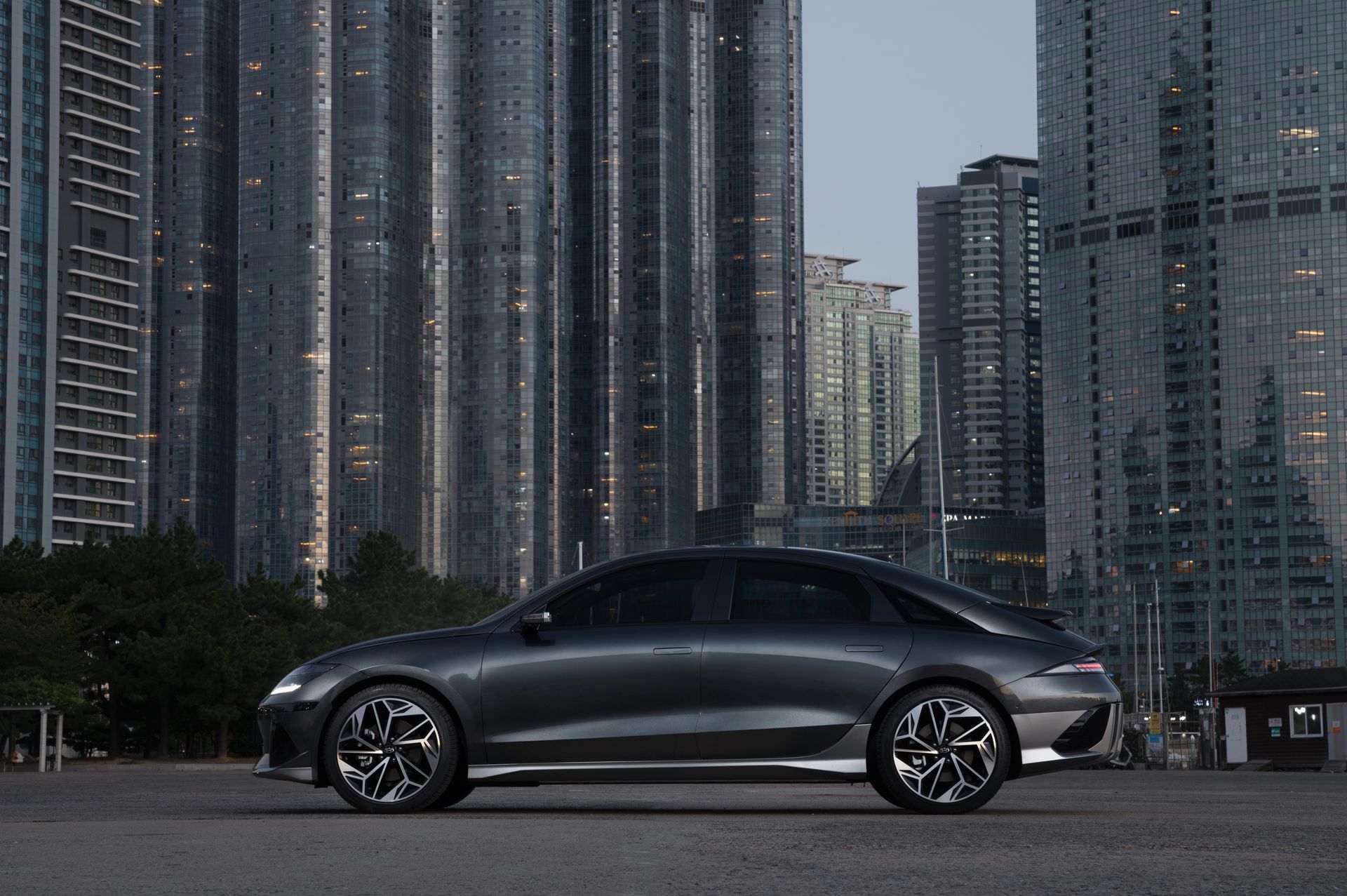 A gray car is parked in front of a city skyline.