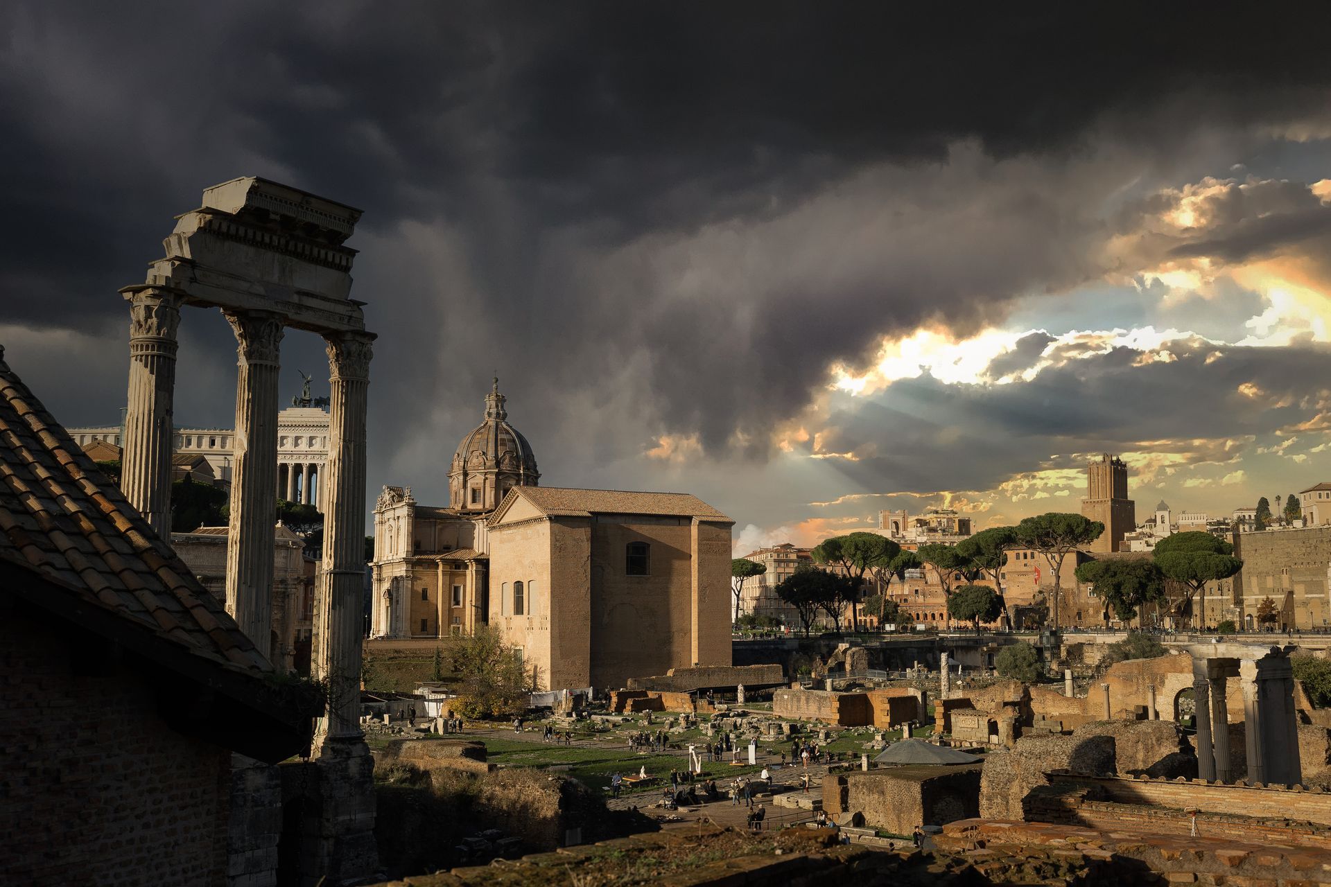 Antiche rovine romane sotto un cielo tempestoso, tra cui colonne, edifici e un tramonto spettacolare.