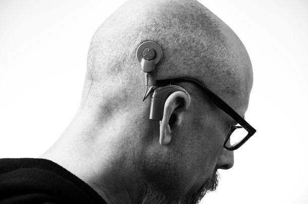 Side profile of a bald man wearing glasses and a hearing device behind his ear