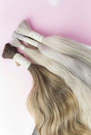 Bundles of hair extensions in various shades of brown, blonde, and grey, tied with white tape on a pink surface.