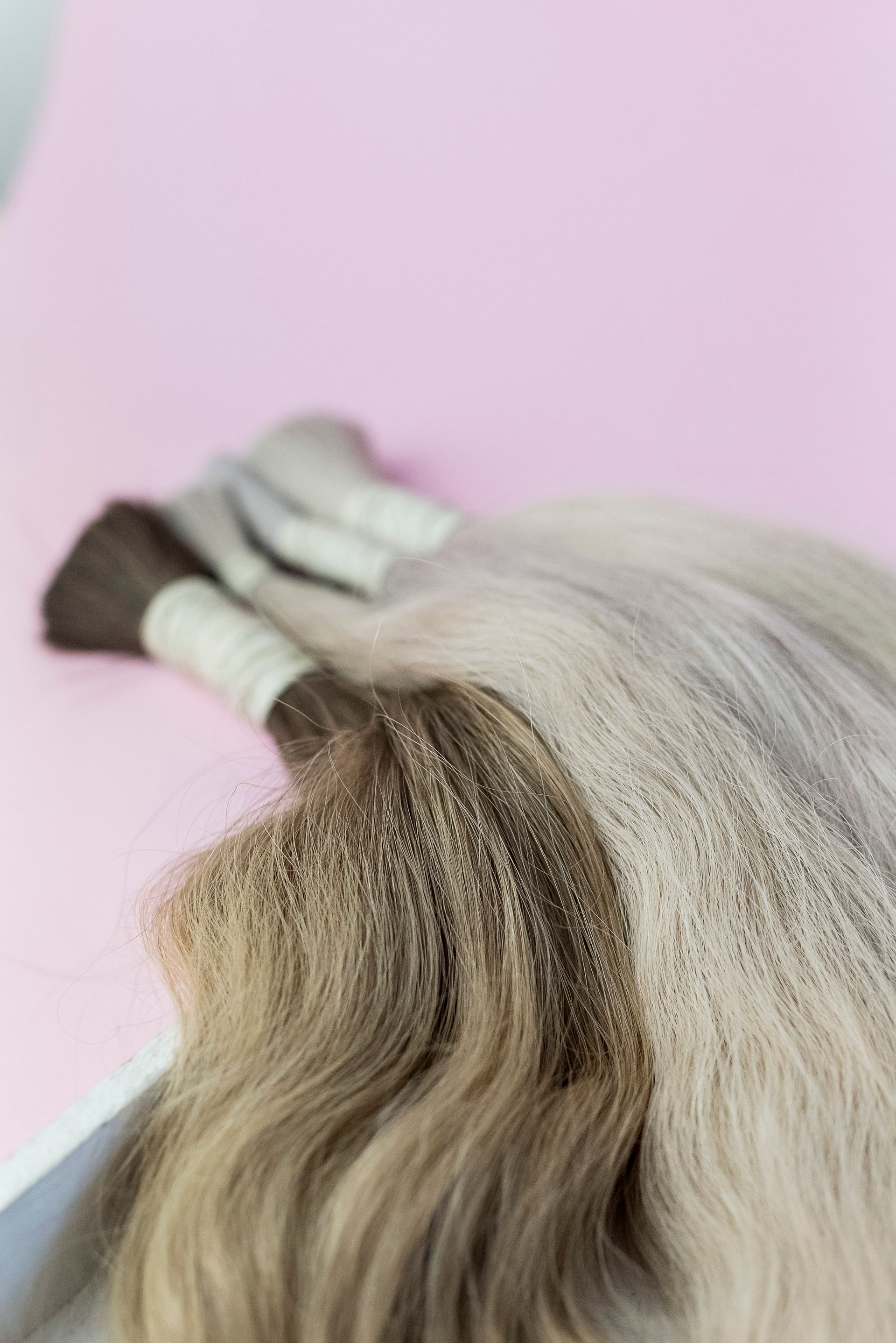Bundles of hair extensions in brown, grey, and blonde on a pink surface.