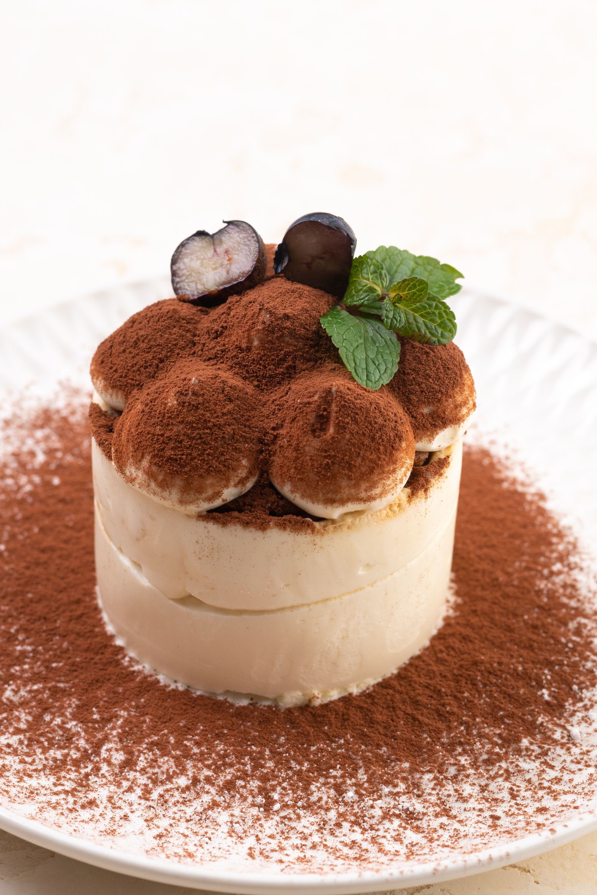 ein kleiner Kuchen mit Schokoladenpulver und Minzblättern auf einem weissen Teller
