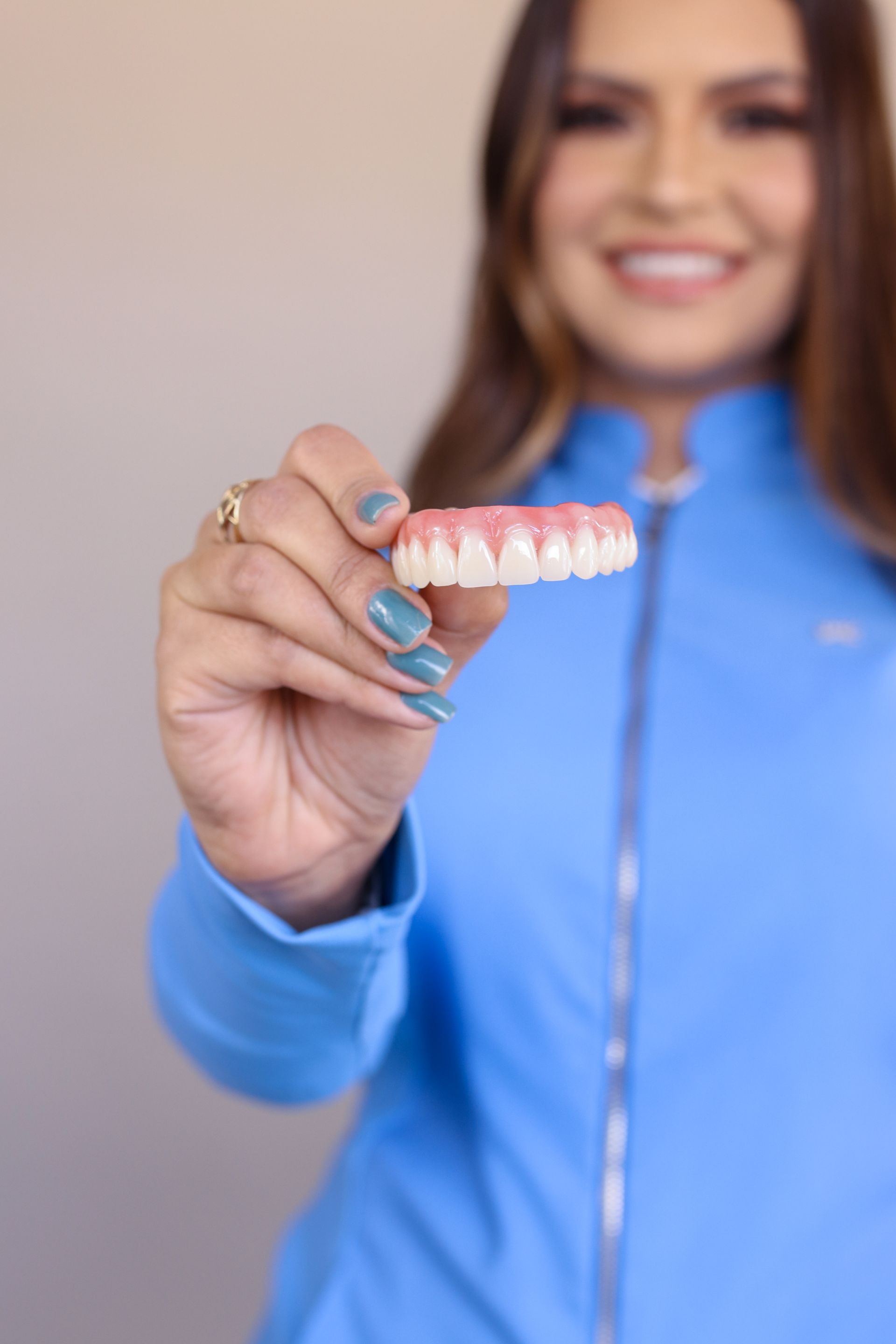 Woman holding a dental prosthesis, smiling, wearing a blue jacket.