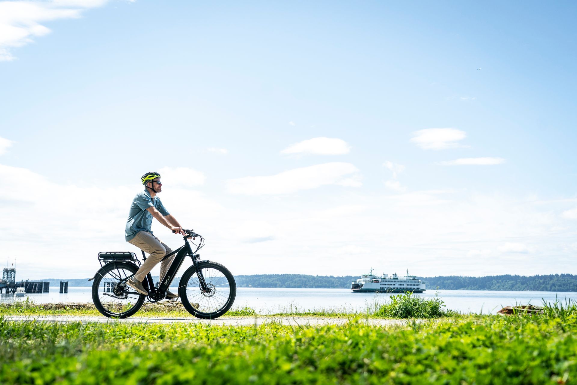 Cyclist riding a bike along a waterfront path on a sunny day