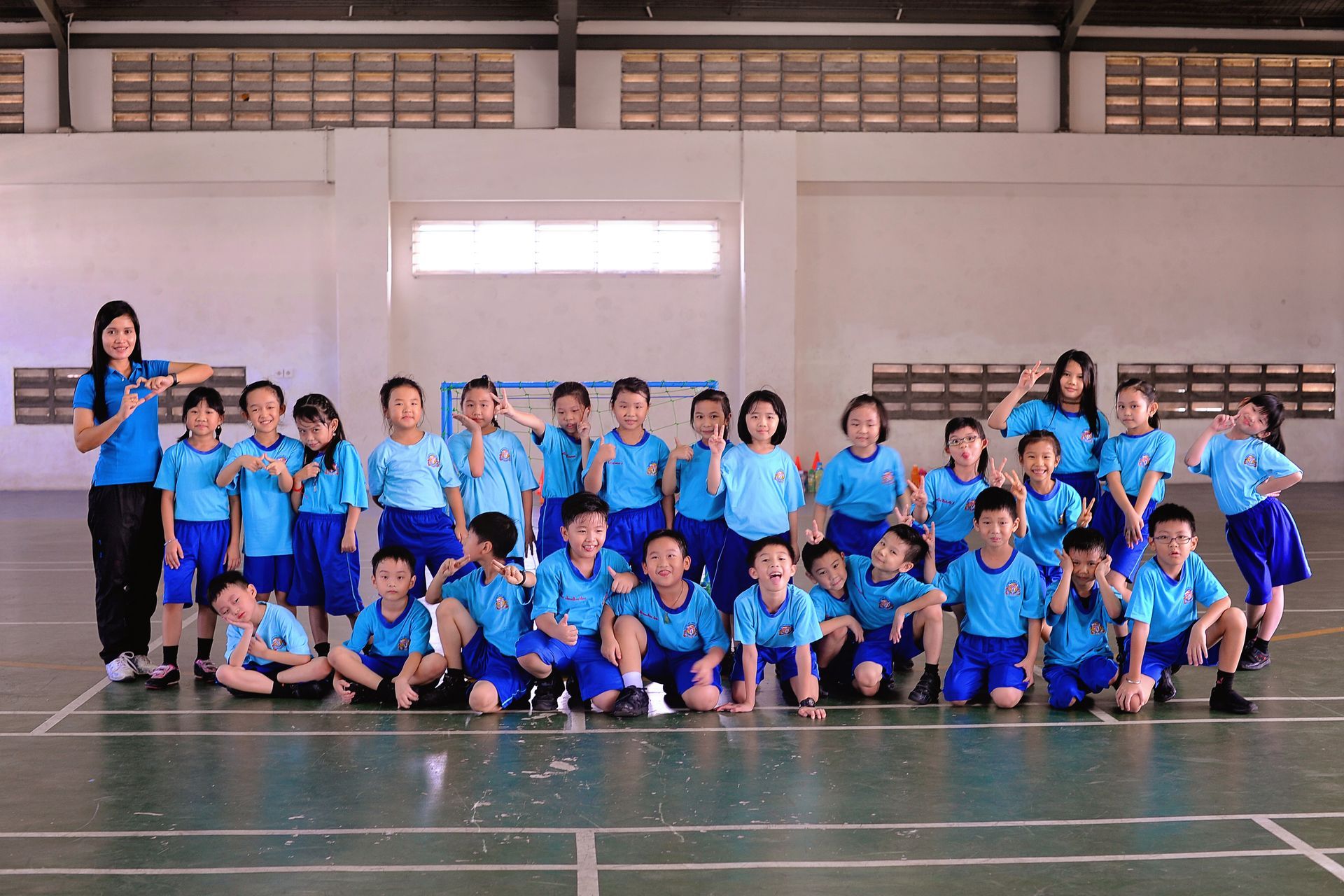 Group of children in blue sports uniforms posing in a gym with a coach on the left