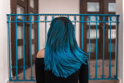 Woman with blue hair in front of a blue railing and brown doors.