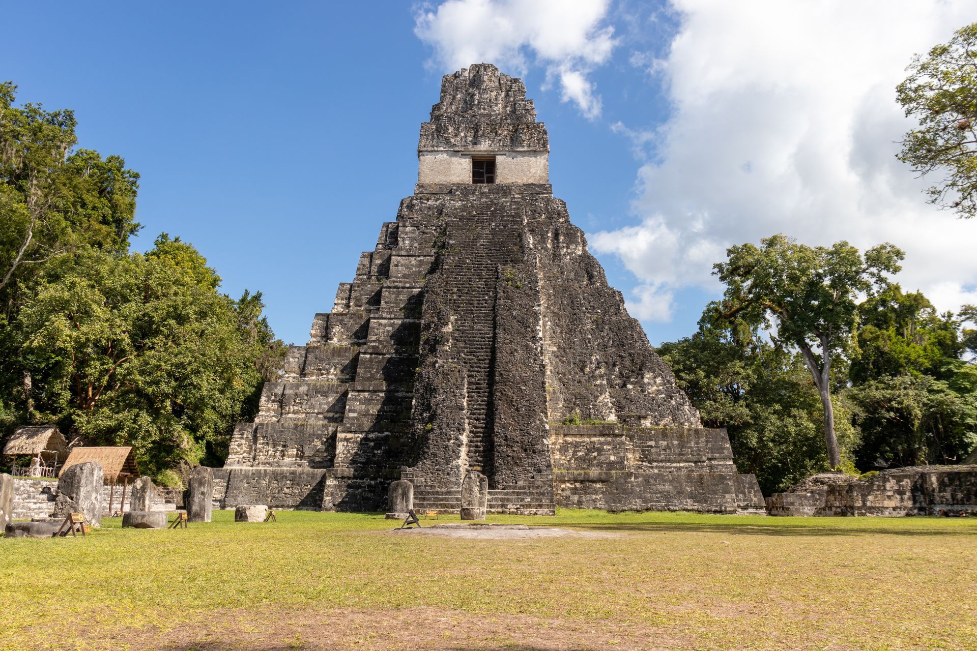 A large stone pyramid is surrounded by trees and grass