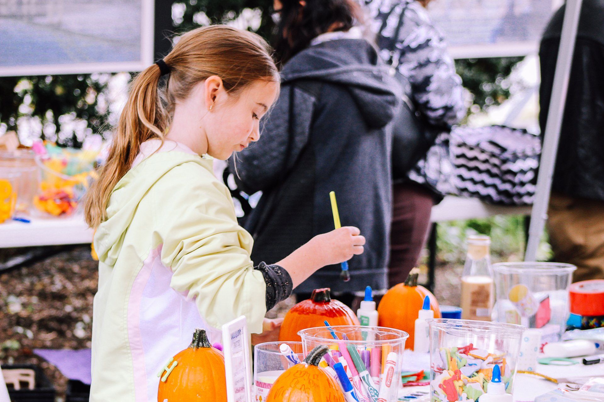 A young girl is sitting at a table painting pumpkins.