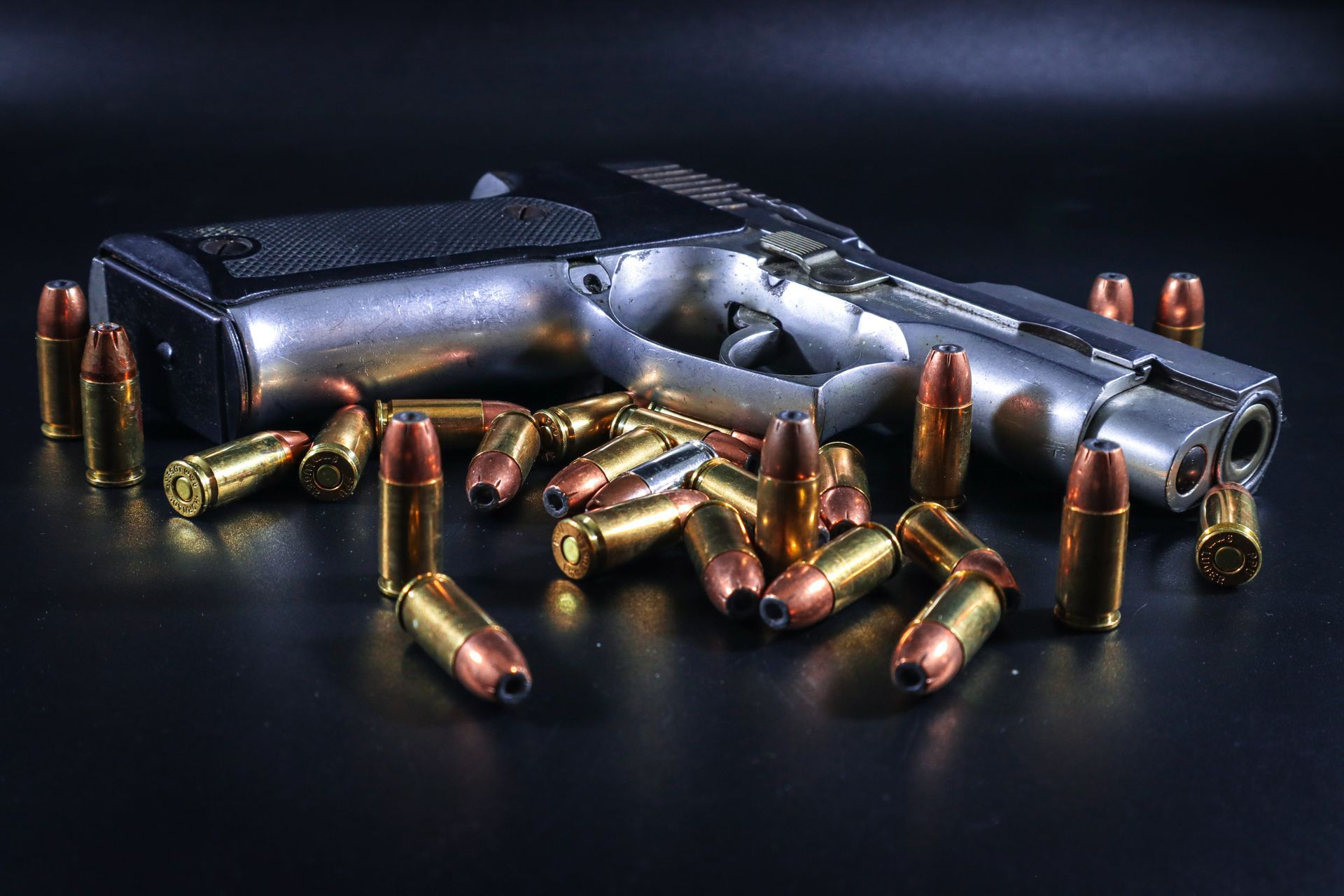 Handgun with scattered brass bullets on a dark surface