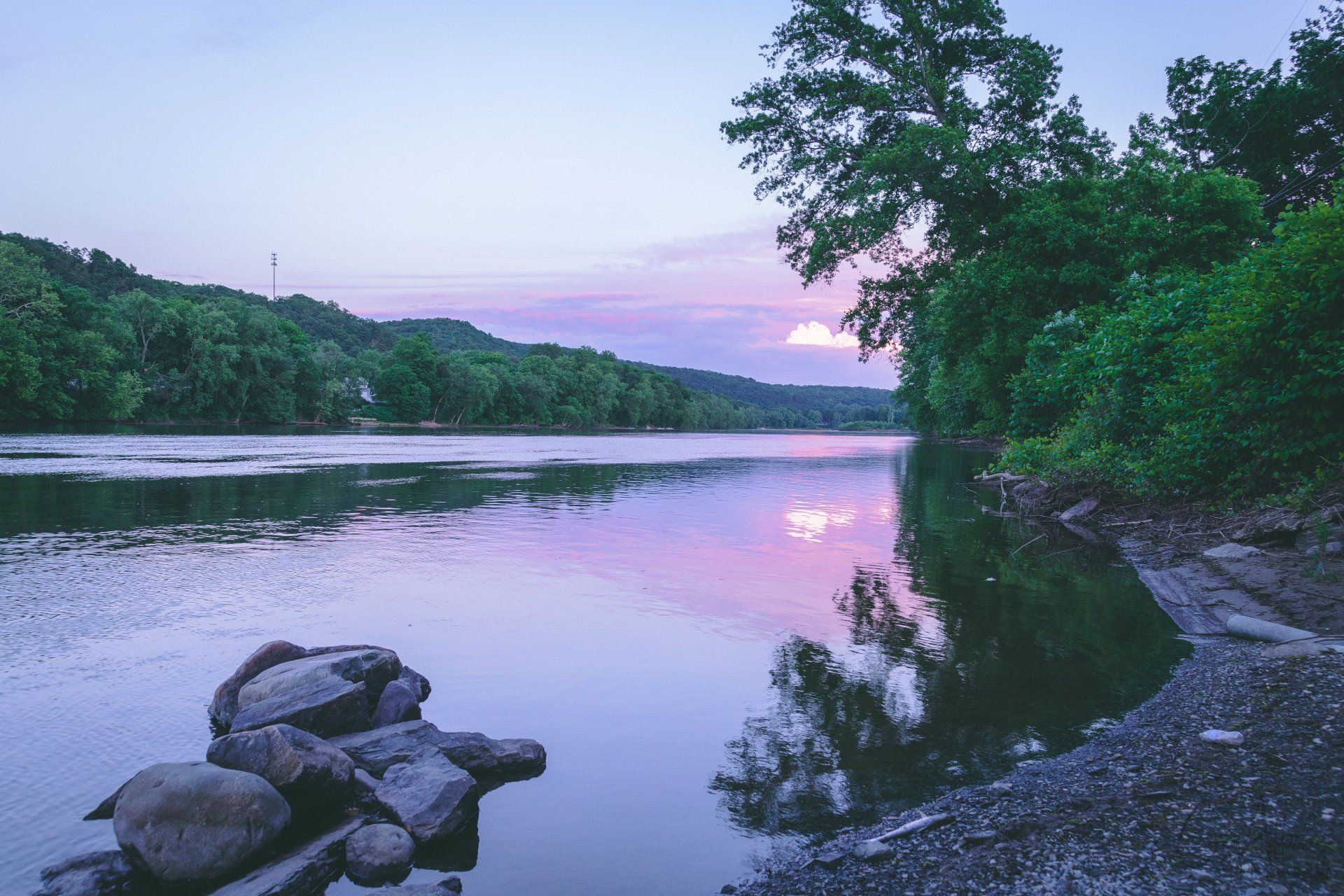 A large body of water surrounded by trees and rocks at sunset.