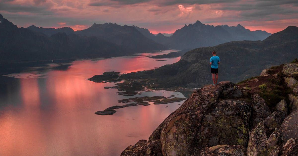 En mann står på toppen av et fjell med utsikt over en innsjø.