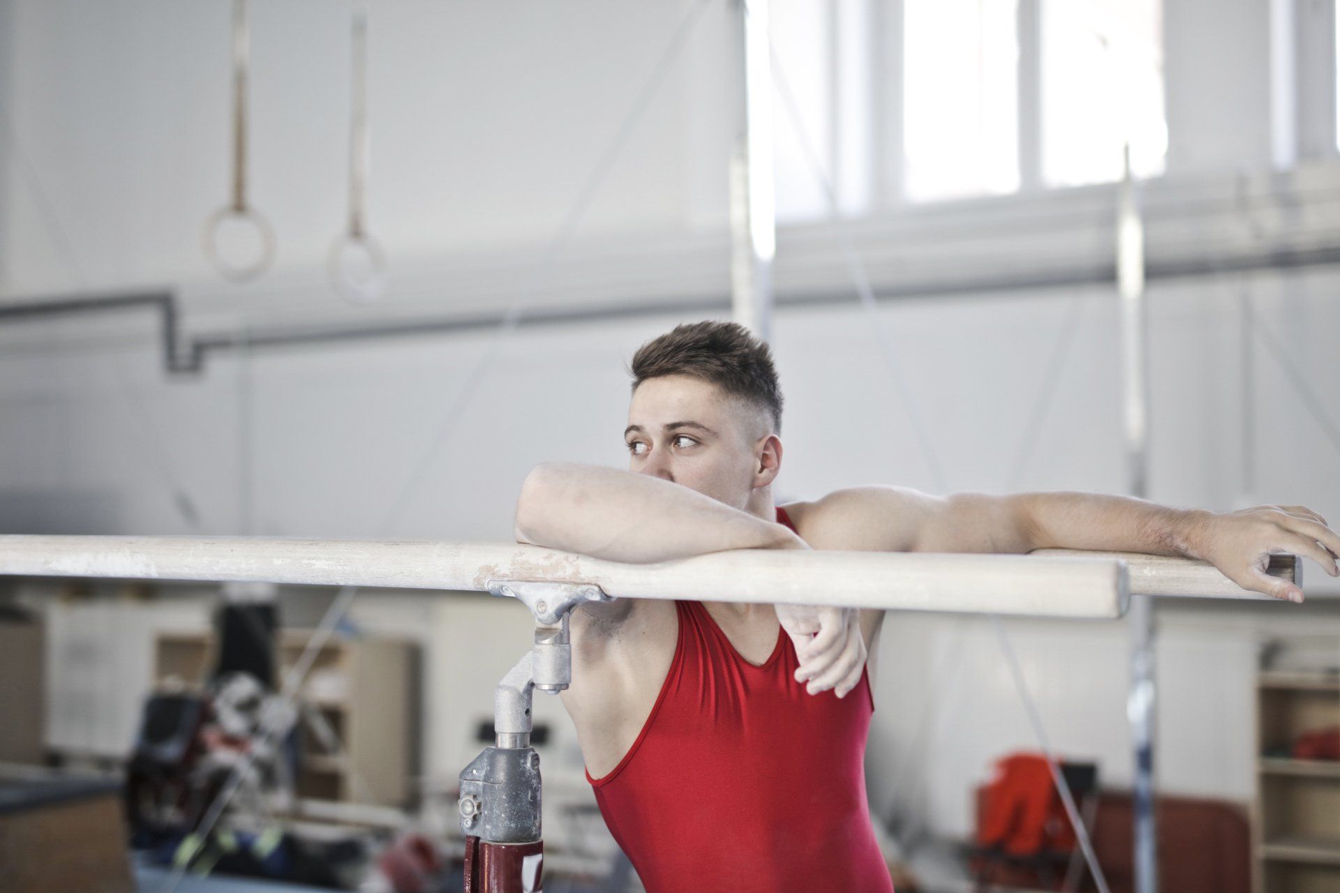 A gymnast is leaning on a bar in a gym.