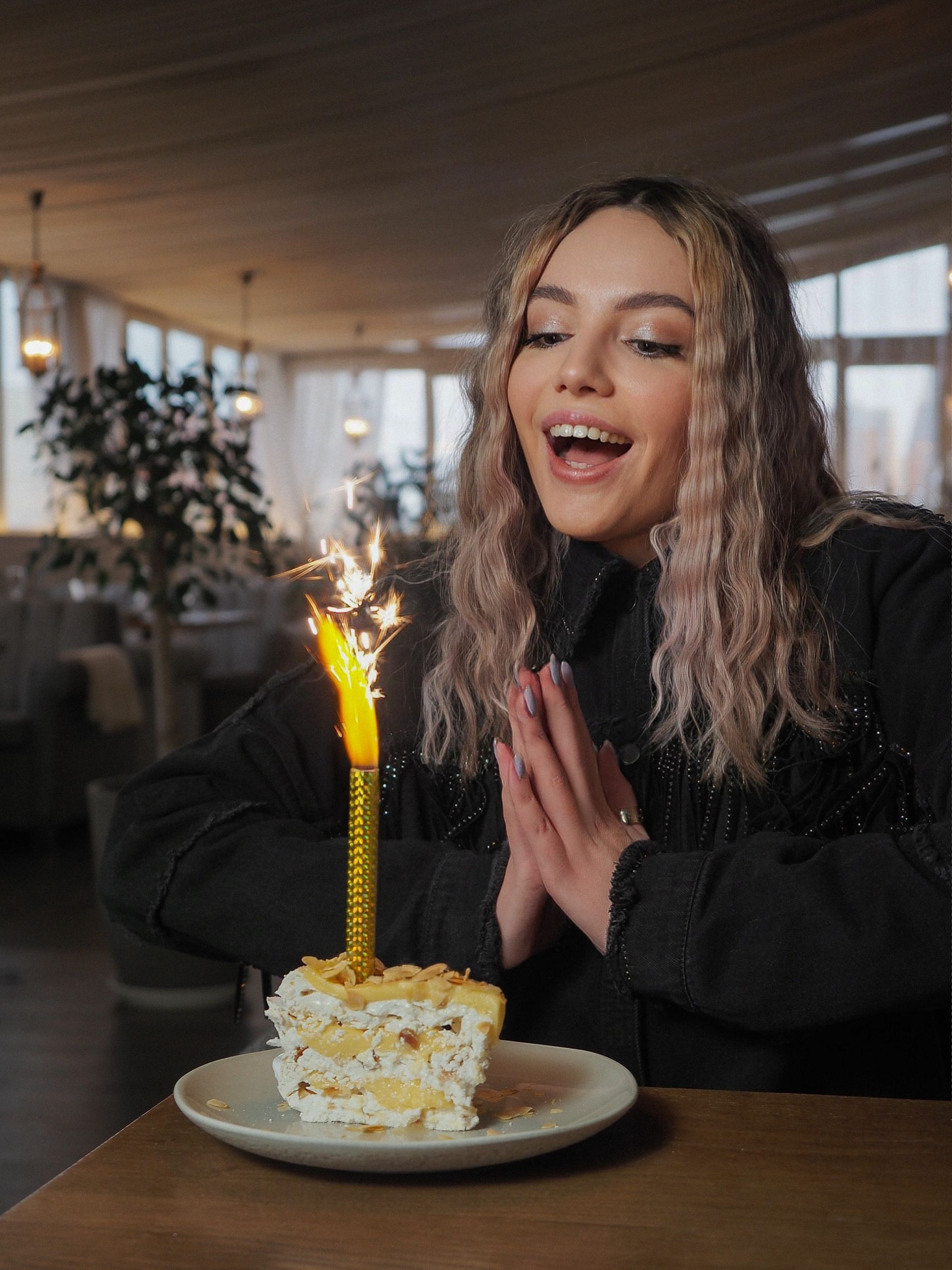 Woman blowing out a candle on a small cake, celebratory expression, restaurant setting.