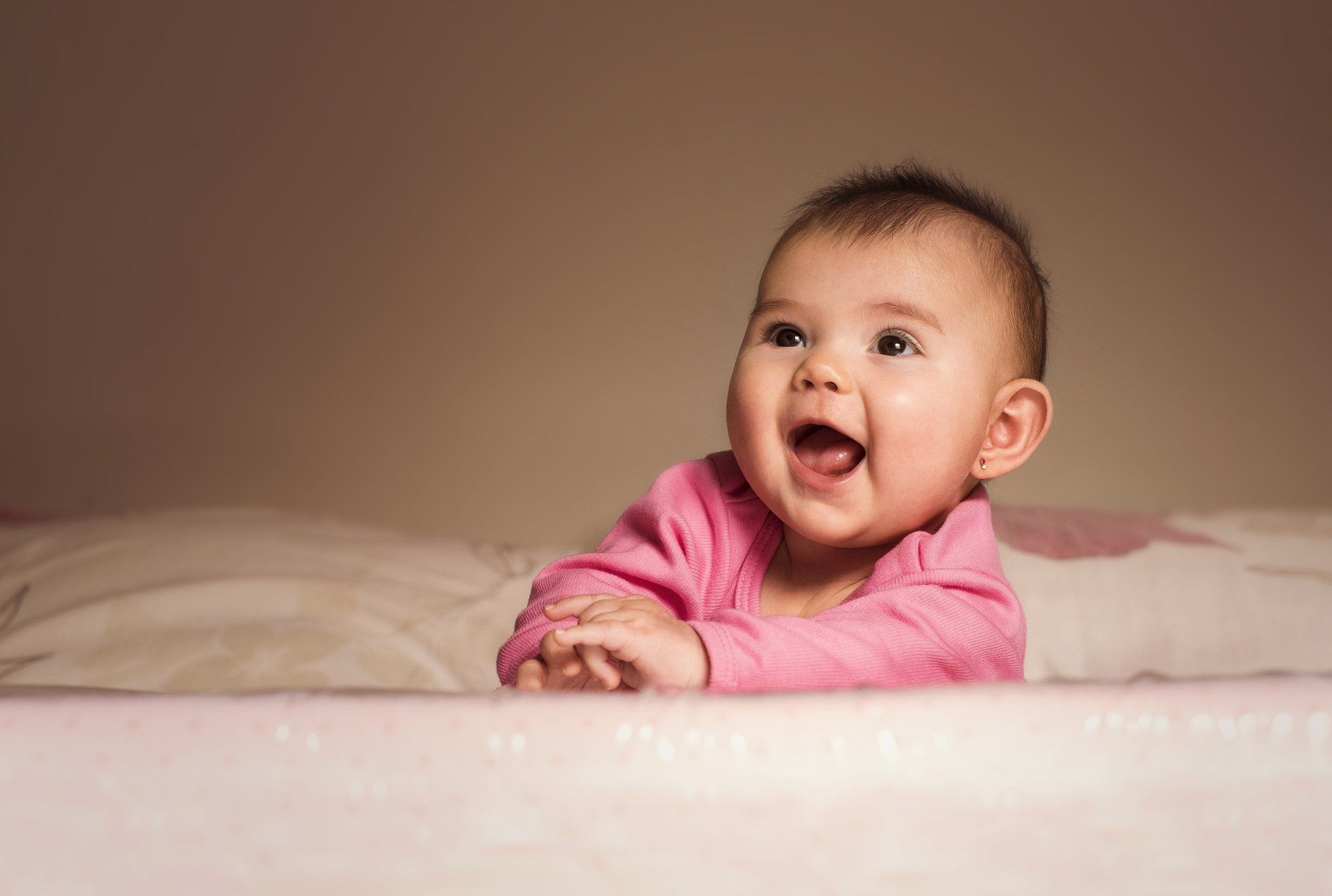 A baby is laying on a bed and smiling.