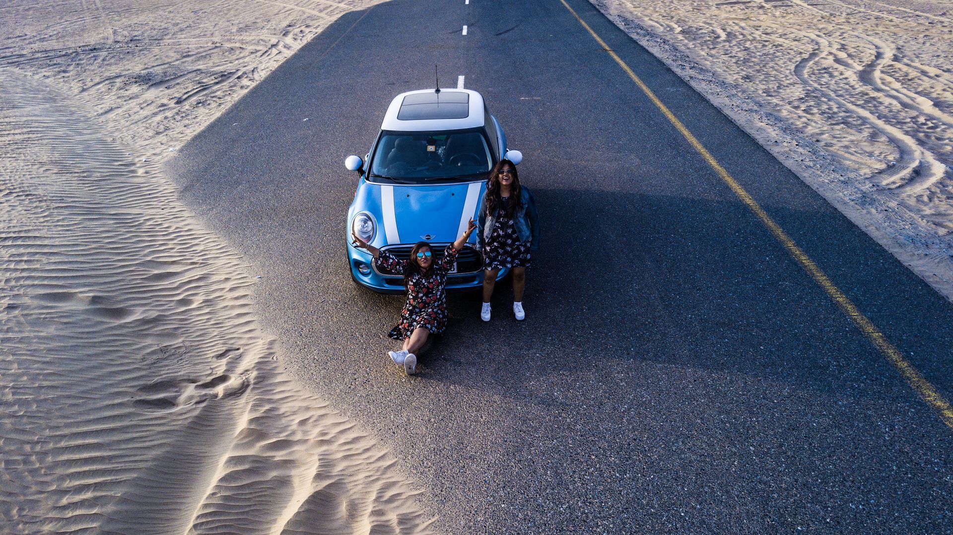 An aerial view of a blue car parked on the side of a desert road.