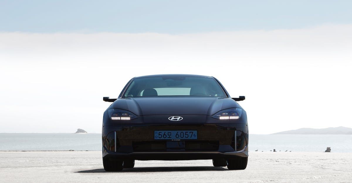 A blue car is parked on a beach next to the ocean. Ioniq6