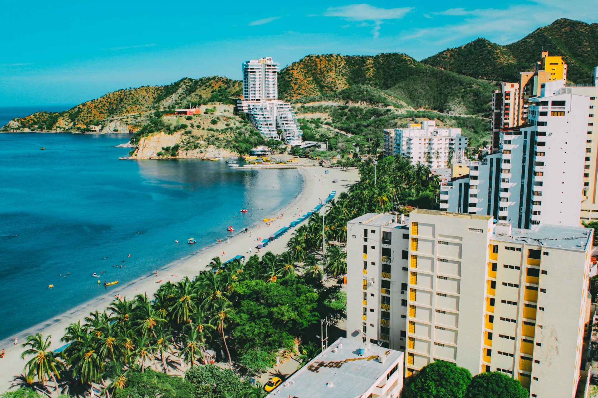 Coastal city with beach, turquoise water, buildings, and green hills.